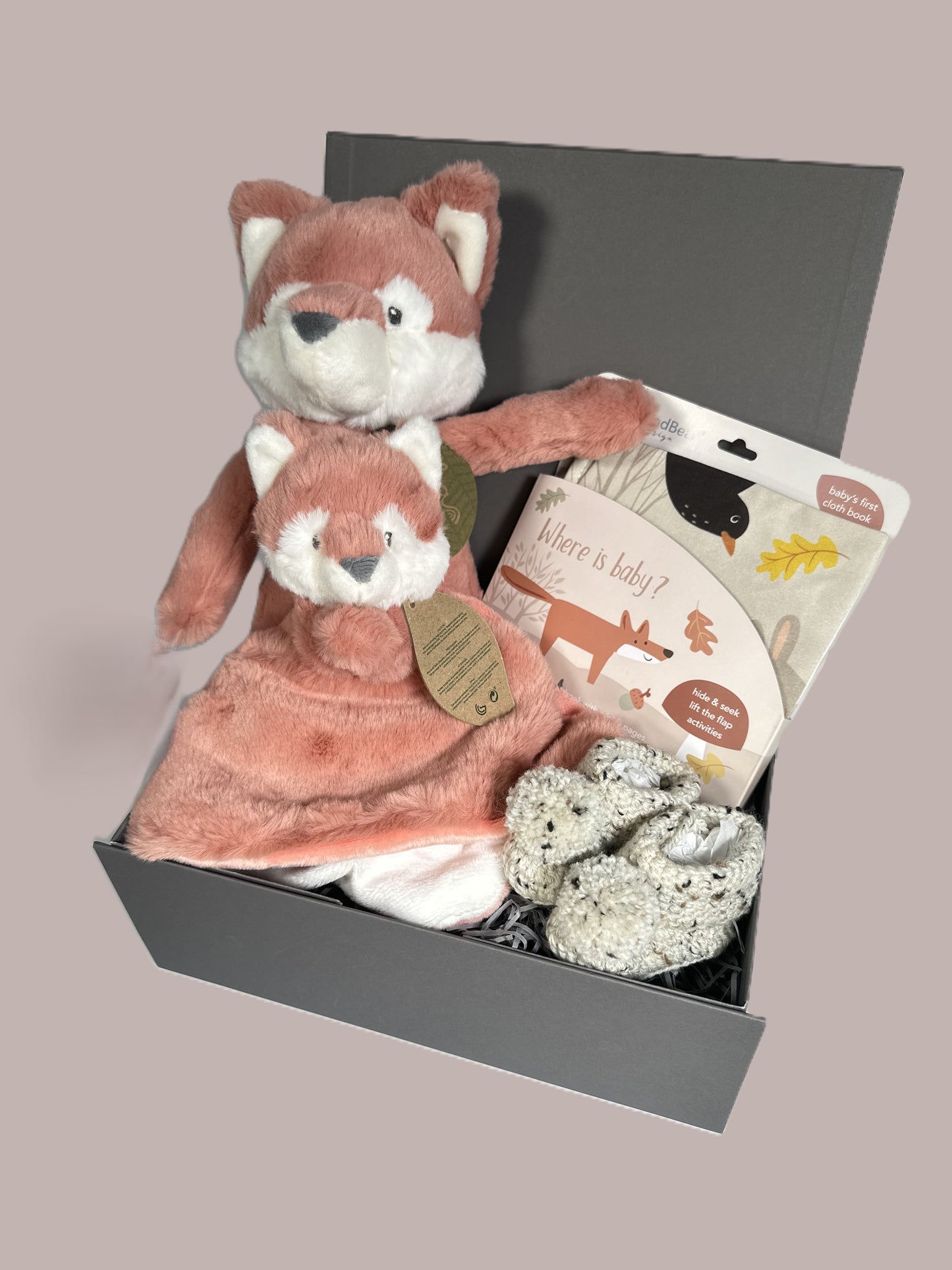 Neutral New Baby shower gift full of eco friendly items including a cloth baby book, an Ebba Fox soft toy and Ebba fox baby comforter, a cotton baby bib and a pair of crocheted baby booties with pompoms.