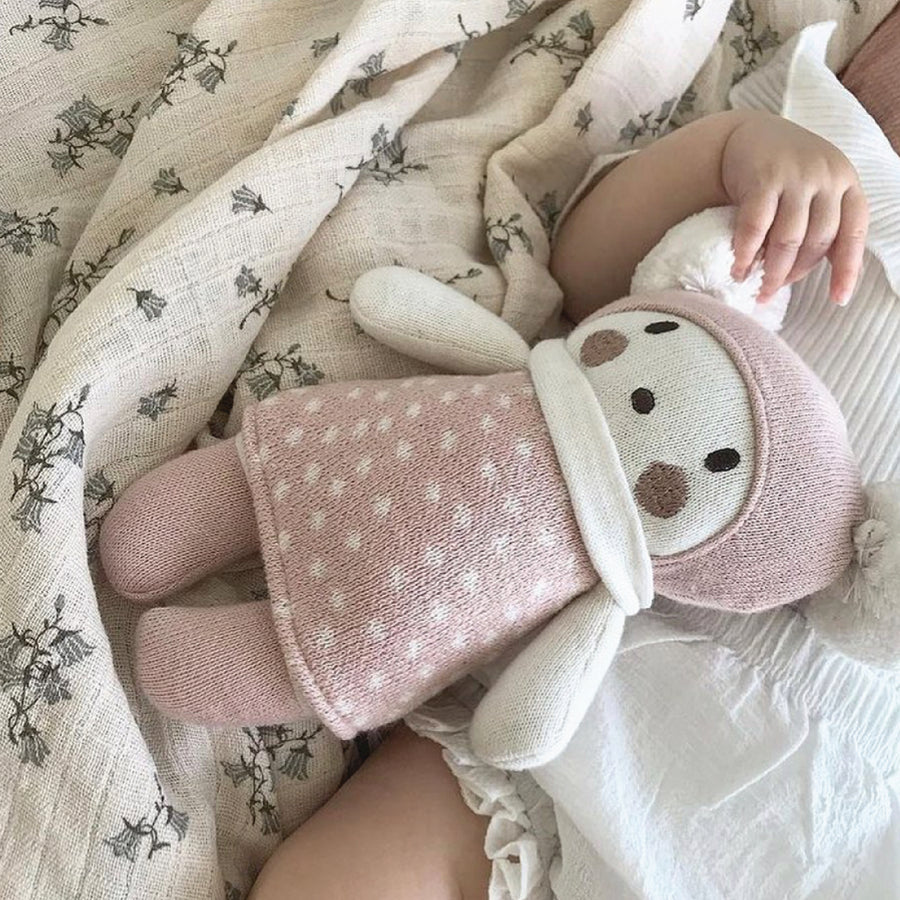 Baby holding a Bella knitted soft baby toy with pink polka dot sleeves on a soft blanket