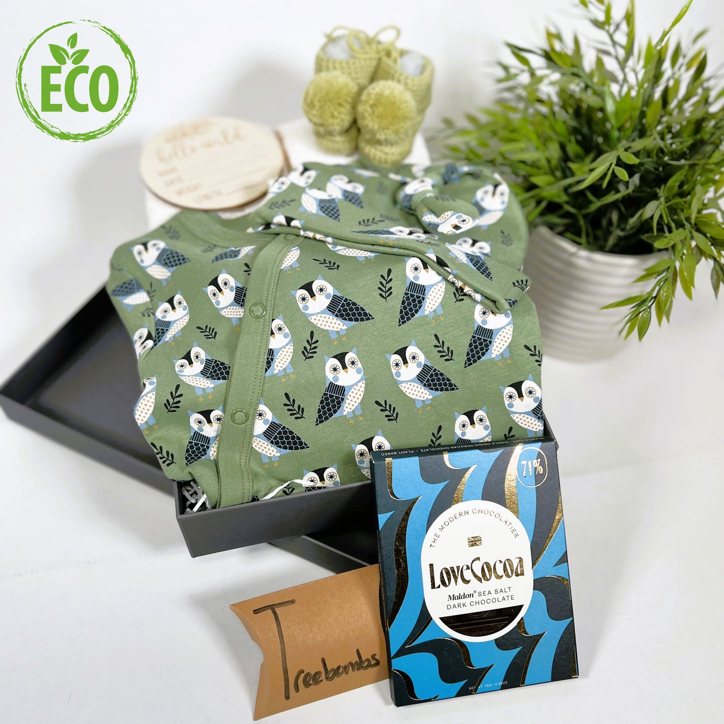 Organic cotton baby romper in green with blue and white owl print, matching baby knot hat, merino wool baby booties with pompom, white cotton cellular baby blanket, baby "Hello world" disc, a bar of Love Cocoa chocolate and baby keepsake box.