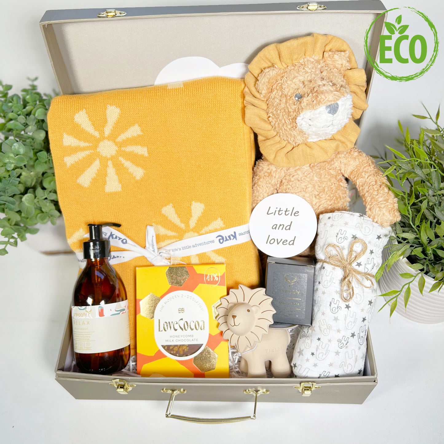 A Baby Keepsake case with eco frindly contents to include a lionel lion soft baby toy, a cotton baby blankey with sunshine knit, a natuarl rubber teething and bath toy lion, a elephant print muslin square , anautral essentail oils candle and shower gel, a bar of Loce Cocoa chocolate and a reversible baby photography disc.