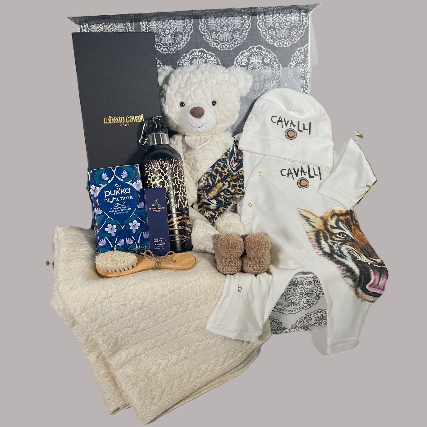 Luxury new parents gift in a baby keepsake box, a Roberto cavelli Tiger baby romper ans matching baby hat, a Roberto Cavelli wtaer bottle, a wooden baby hair brush and comb st, a cream cashmere baby blanket, a pair of merino wool baby booties.