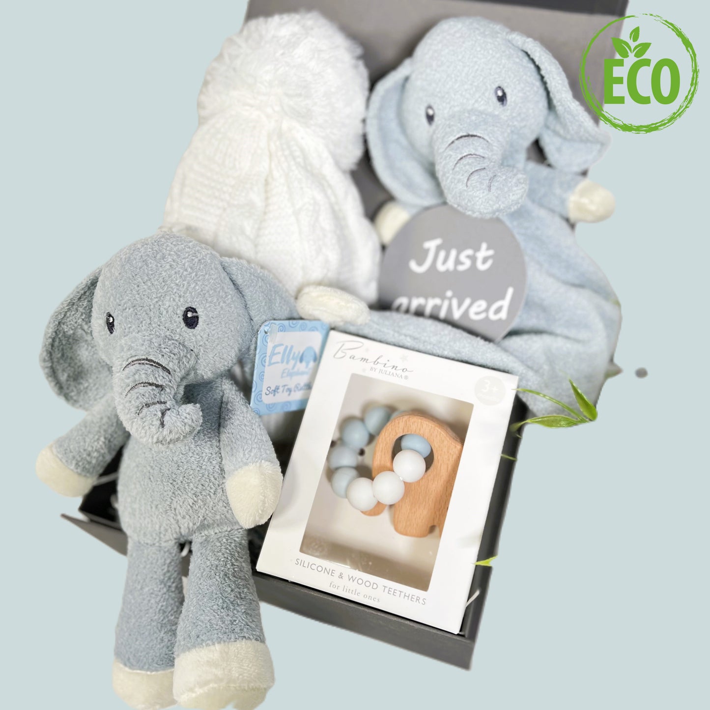 Blue and white new baby boy hamper contained in a grey baby keepsake box, a Blue and white elephant rattle toy with embroidered eyes and trunk and a matching Ely elephant baby blankie comforter. A white baby pompom hat made from recycled plastics, a "Just arrived" baby photography disc and a Bambino silicone and beech wood baby teether in blue and white with a wooden elephant shaped teether.
