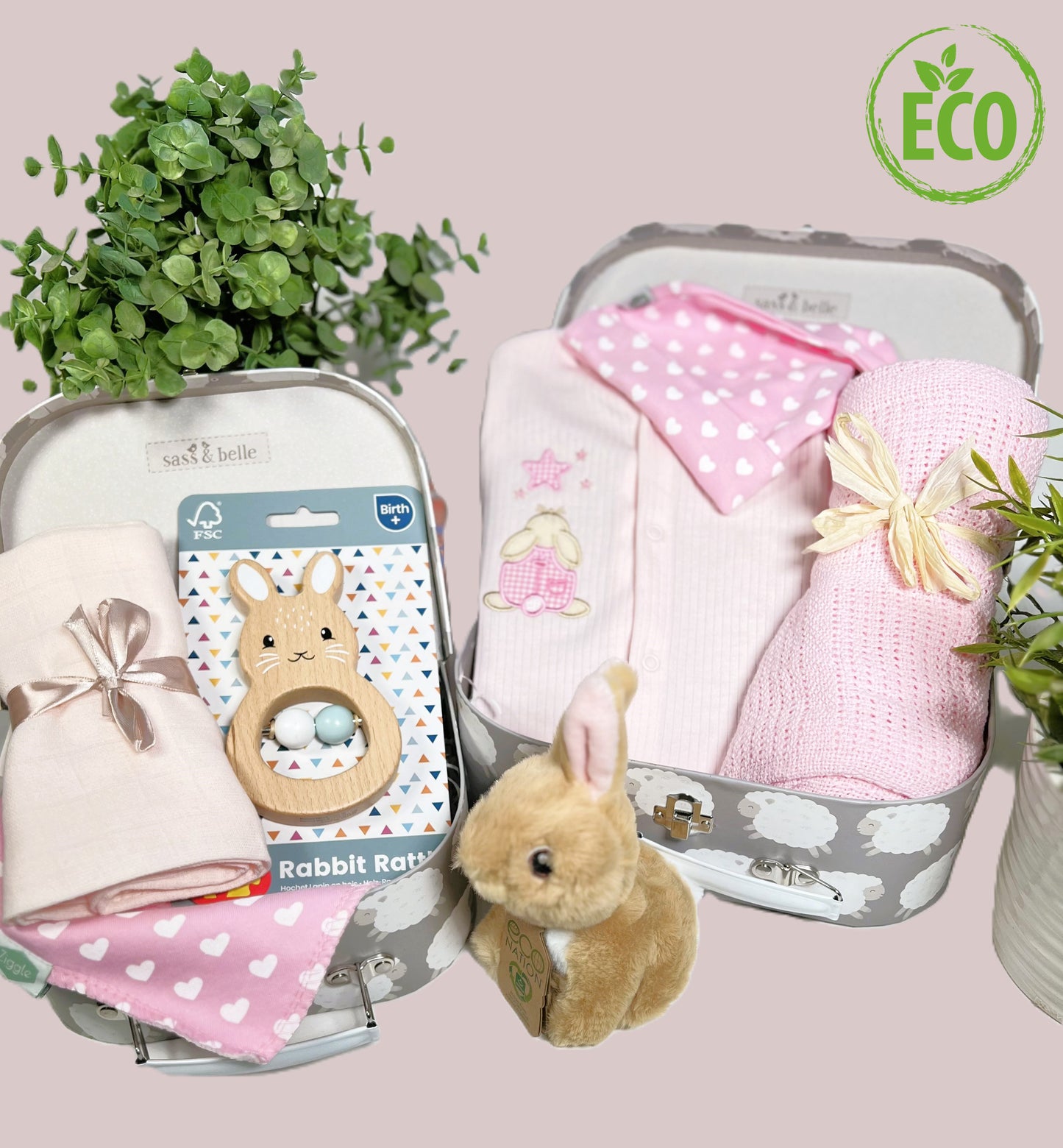 Eco Friendly pink and white baby girl gift contains a pink cotton ribbed baby sleepsuit wit an applique rabbit looking at a star, a pink cotton cellular baby blanket,a FSC wooden bunny shaped baby rattle, an eco friendly bunny soft toy, a coton baby bib and matching baby knot hat and 2 baby keepsake cases.