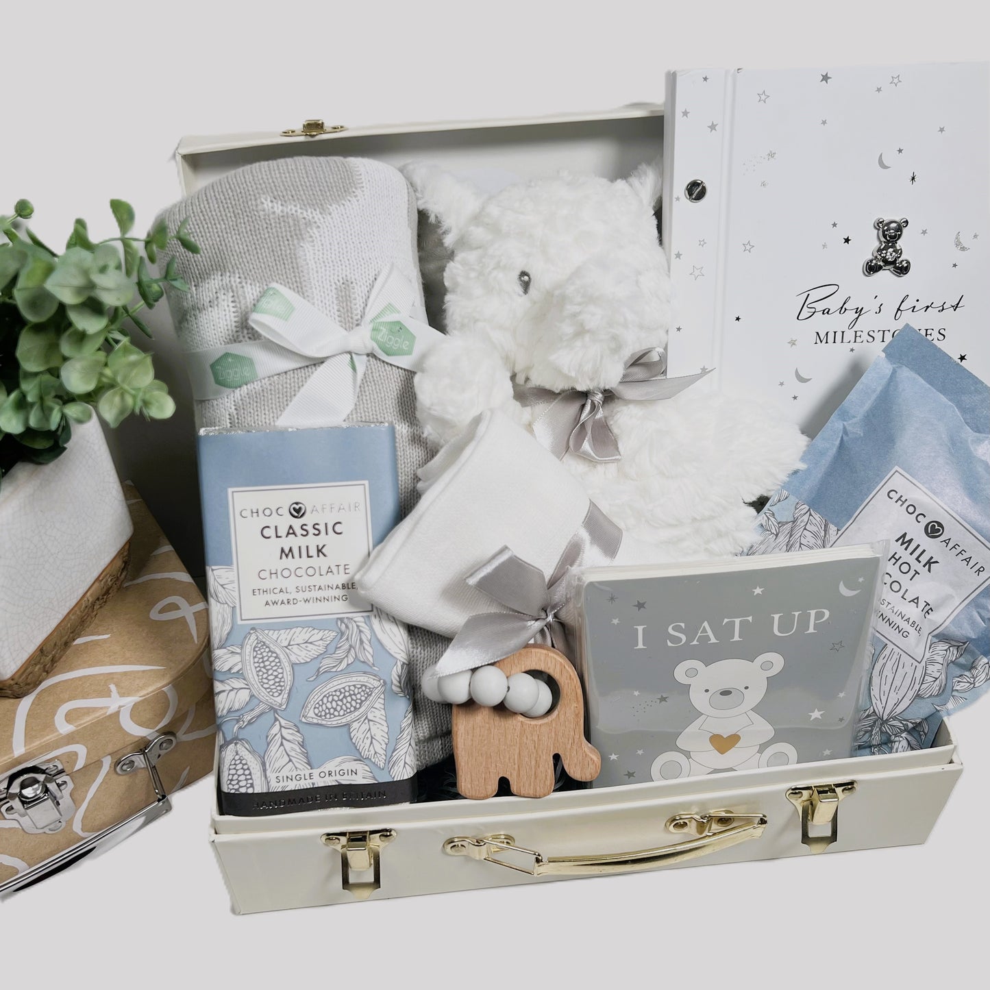 This is a luxury baby hamper in a cream baby keepsake case with gold coloured fittings containg a Mary Meyer Elephant soft Baby toy, a Ziggle cotton baby blanket in a grey and white safari animal print, a Bambino baby phote album with foiled baby milestaone cards, a bambinoo elephant baby teether,a large white baby muslin square, a 90gr bar of Choc affair milk chocolate and a 200g pouch of Choc Affair hot chocolate.