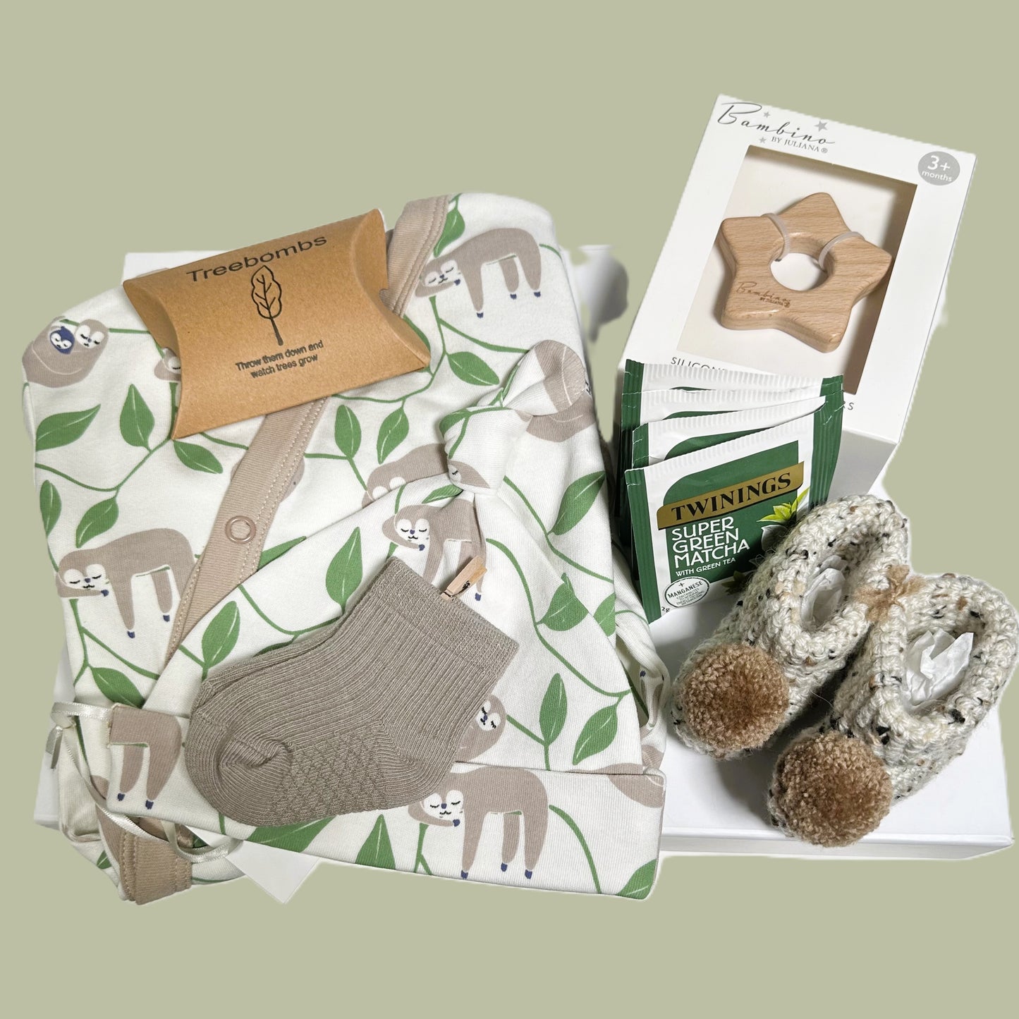 Baby shower gift containing a sloth print baby sleepsuit and baby knot hat, soft, crocheted baby booties, a pair of cotton sock in taupe ,Bambino star teether and some Matcha teabags. All in a white baby keepsake box.