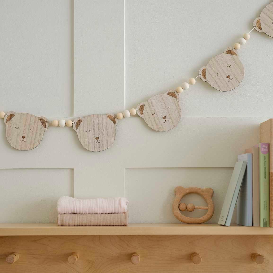 Wooden bear head garland on a shelf with books and baby items against a light green wall.