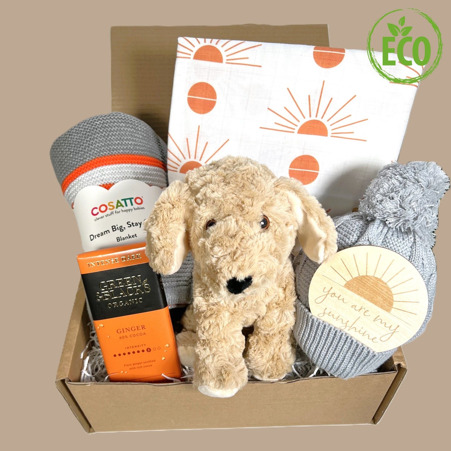 Unisex new baby gift hamper box containng a grey, white and orange striped cotton baby blanket, a 110cms x b 110cms white muslin baby blanket with an orange sunshine print, a grey baby pompomh hat made fro 50% recycled plastics, a round wooden plaque with the text "You are my sunshine" , a bar of Green and Blacks organic ginger chocolate and a eco friendly cockapoo baby puppy toy made from recycled plastics.