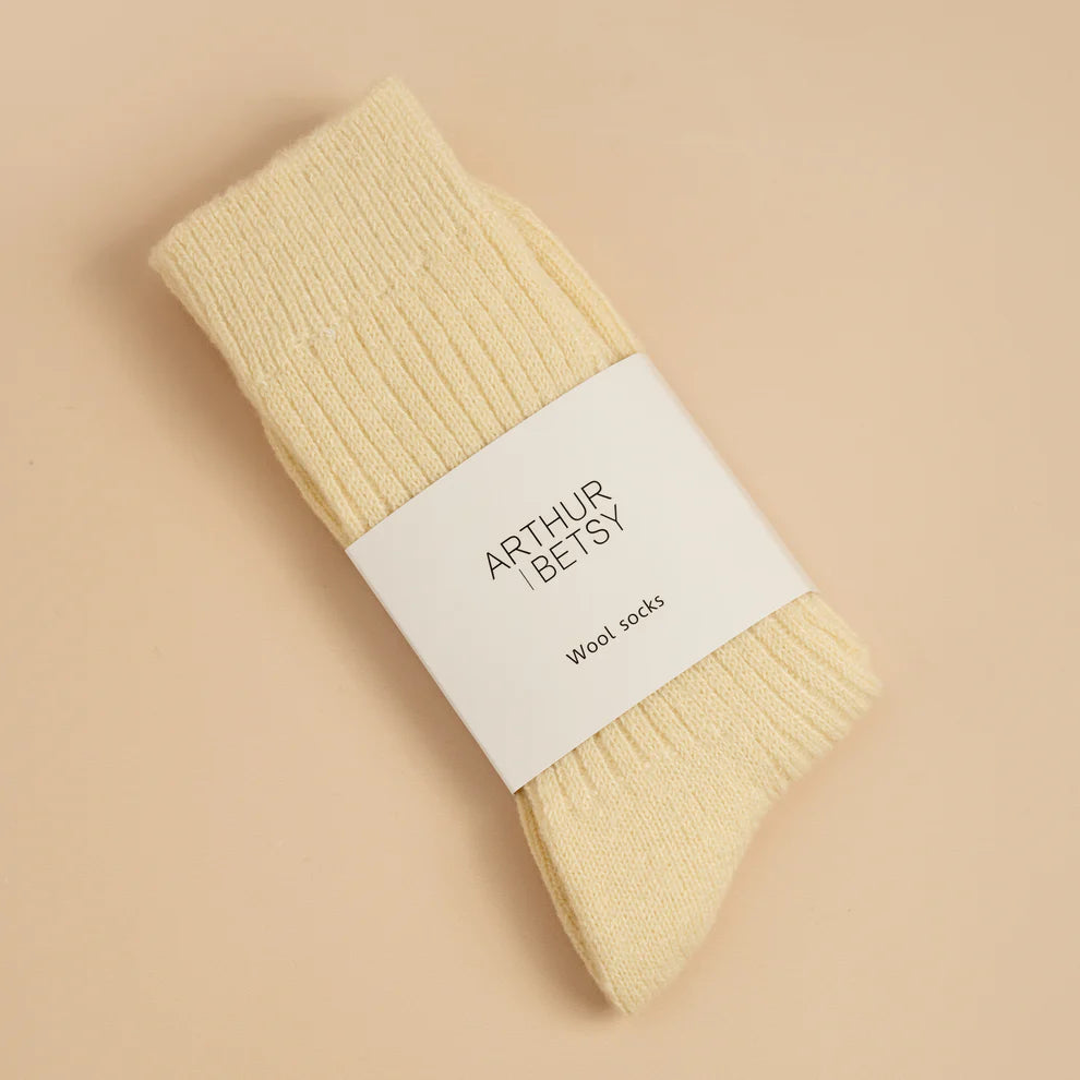 Pair of cream alpaca wool socks with a white label on a beige background
