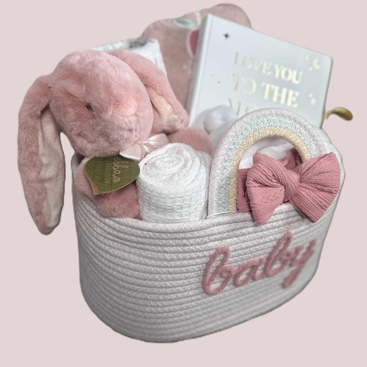 Baby gift basket with plush bunny soft baby toy, baby photo album, and baby haedband on a pink background
