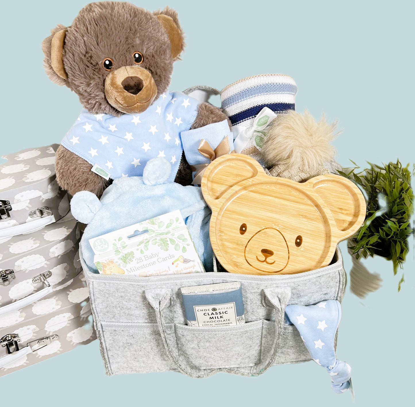 Nappy Caddy new baby boy gift in a grey felt nappy caddy with thre compartments and six pockets containing a large brown bear soft toy made from recycled plastics, a bamboo baby plate with bear face, a blue hooded baby dressing gown, a pack of baby milestone cards, baby pompom hat, a blue baby muslin square, baby toiletries and a Love Cocoa bar of chocolate.