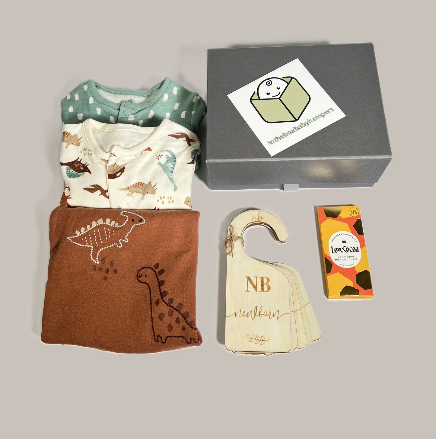Baby boy hamper in a grey magnetic baby keepsake box containing a set of three dinosaur pint baby body suits in cotton, a lovely little bar of Love cocoa chocolate and a set of wooden baby wardrobe dividers.