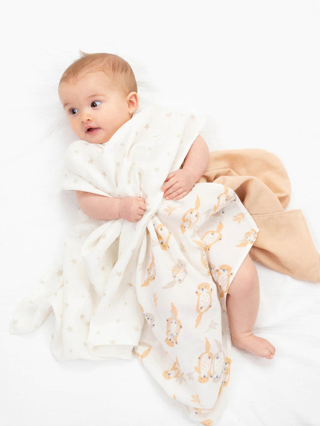 3 Double layer muslin fabric GOTS certified organic cotton baby muslins 60cms x 60cms . 1 in white with a pale orange and ecru otter print, one pale orange and 1 white with ecru star print, a white cotton cellular baby blanket, a biscuit coloured baby pompom hat and a packet of Twining "Sleep" teabags.
