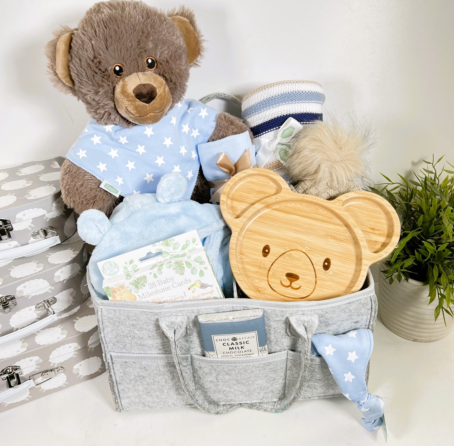 Nappy Caddy new baby boy gift in a grey felt nappy caddy with thre compartments and six pockets containing a large brown bear soft toy made from recycled plastics, a bamboo baby plate with bear face, a blue hooded baby dressing gown, a pack of baby milestone cards, baby pompom hat, a blue baby muslin square, baby toiletries and a Love Cocoa bar of chocolate.