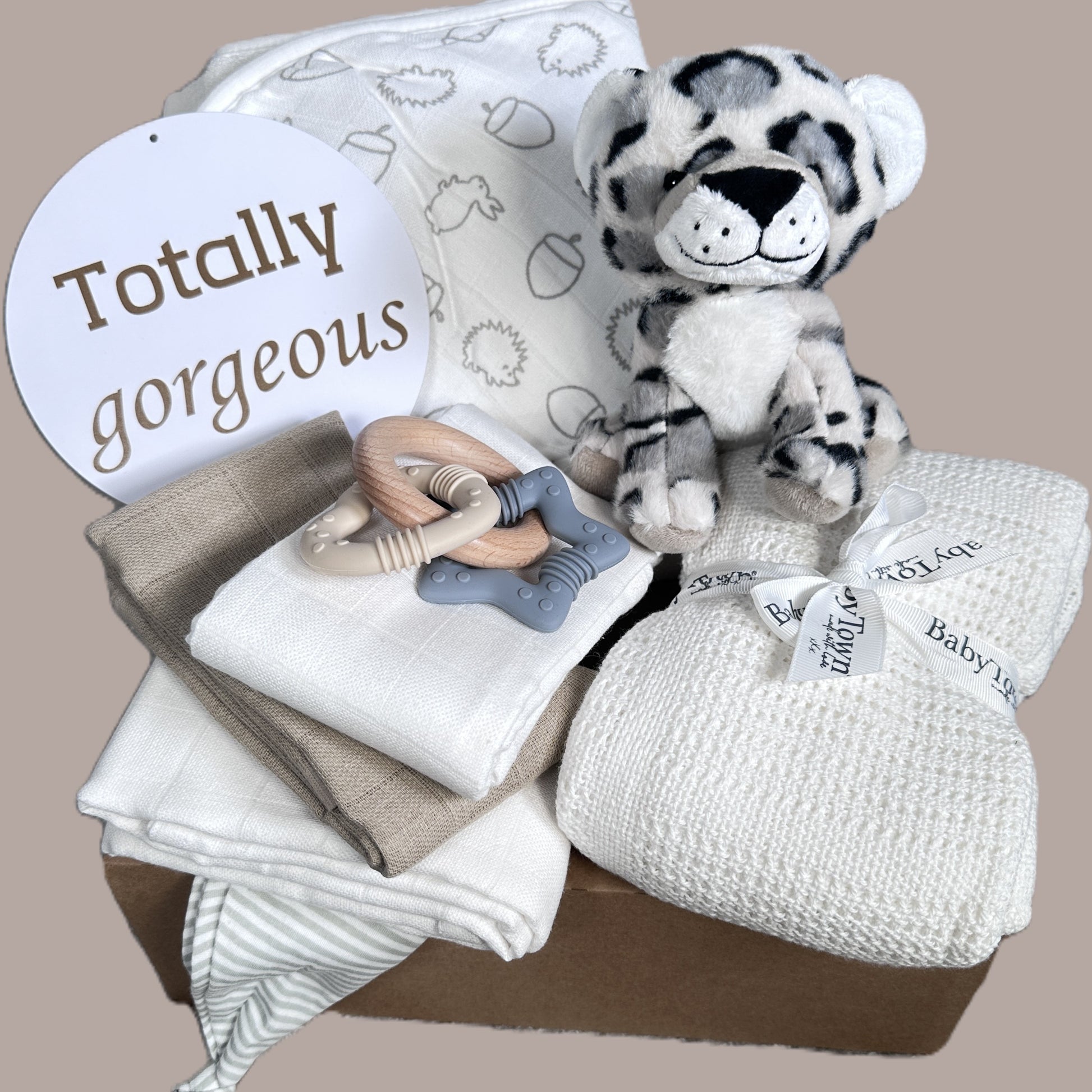 Baby gift basket with plush toy, blanket, and teether on a beige background