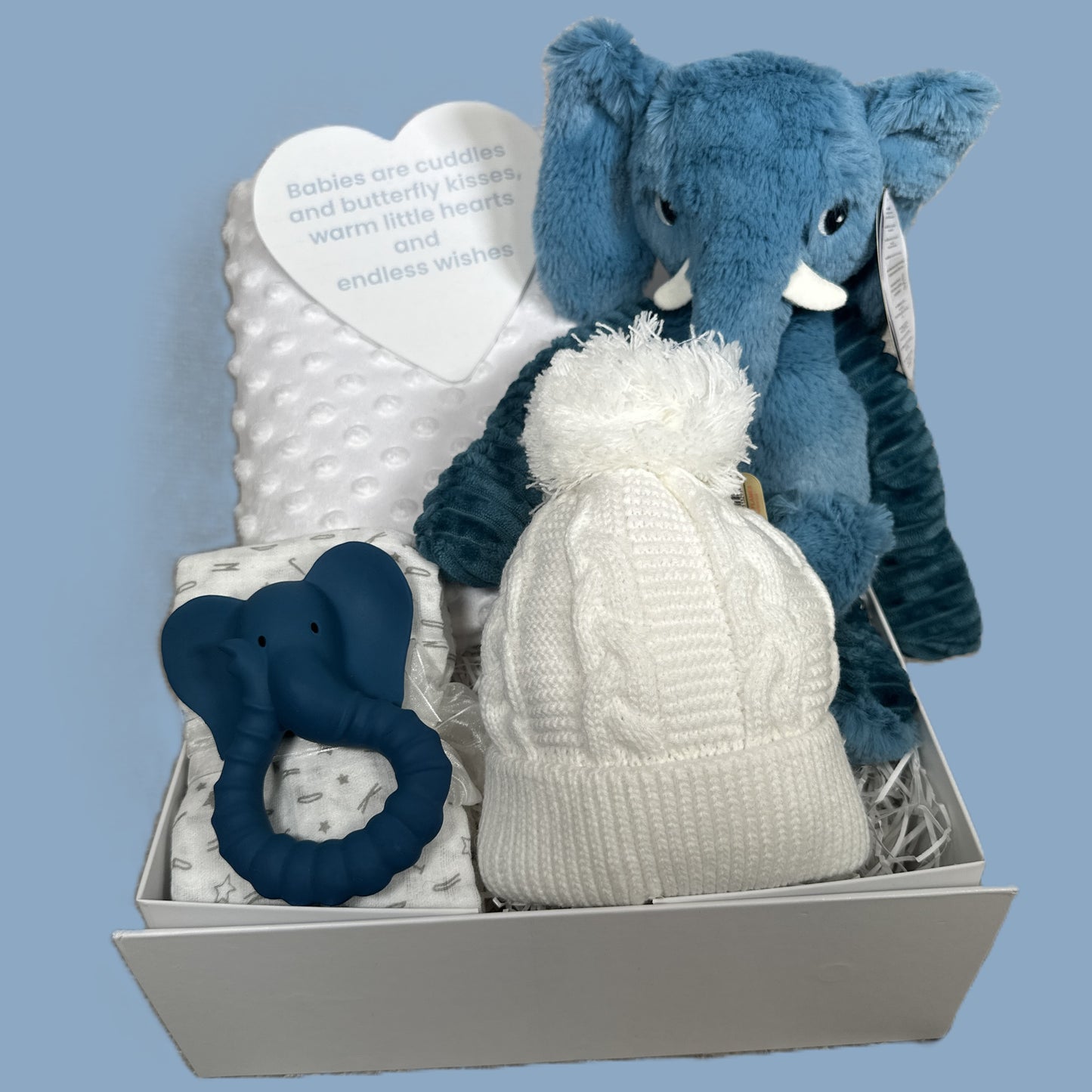 Baby gift set with blue elephant plush toy, white blanket, and teething ring on a light blue background
