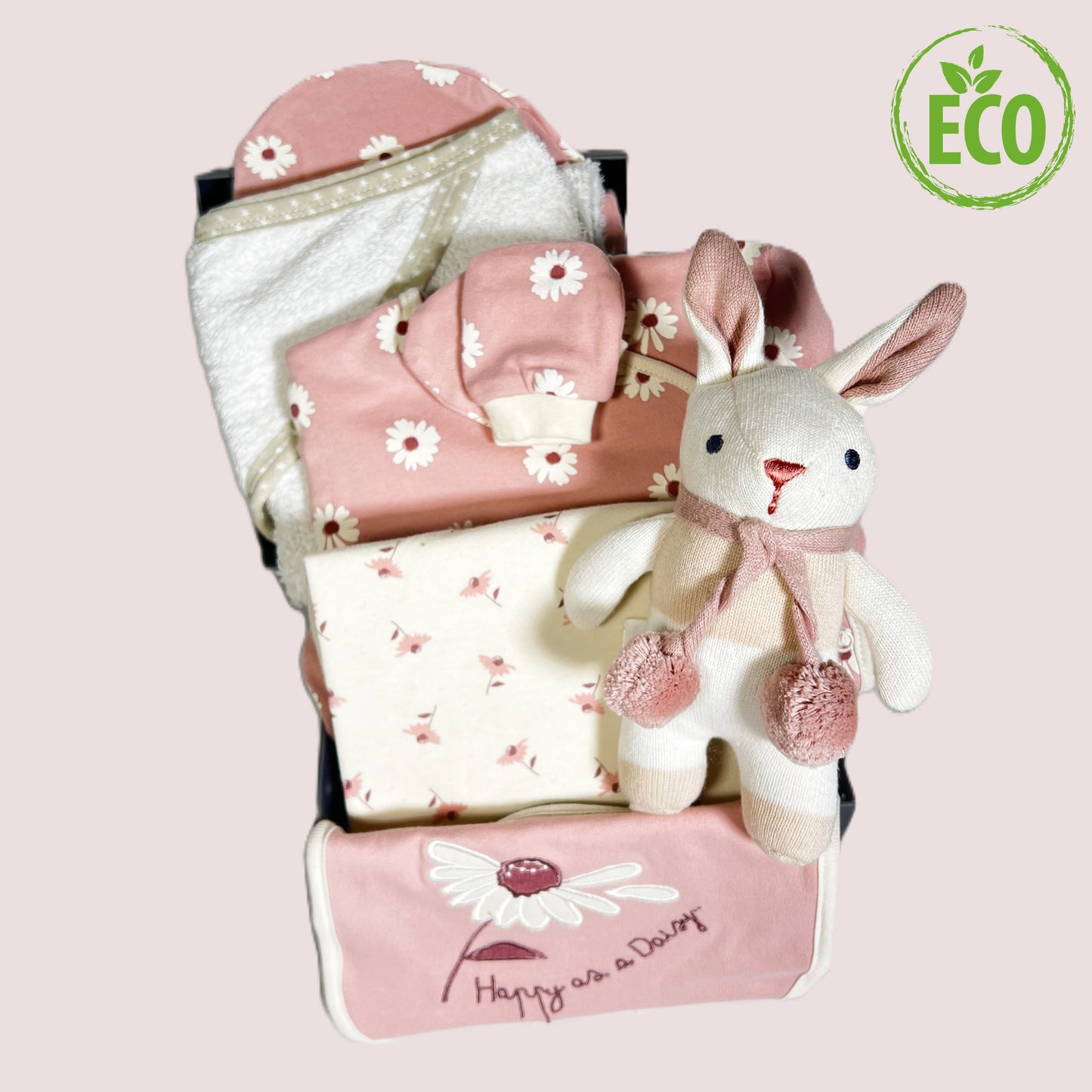 A new baby girl hamper in a grey baby keepsake box containing a pink and white organic cotton layette set with a white daisy print, a cotton hooded baby towel and an organic cotton bunny baby rattle.