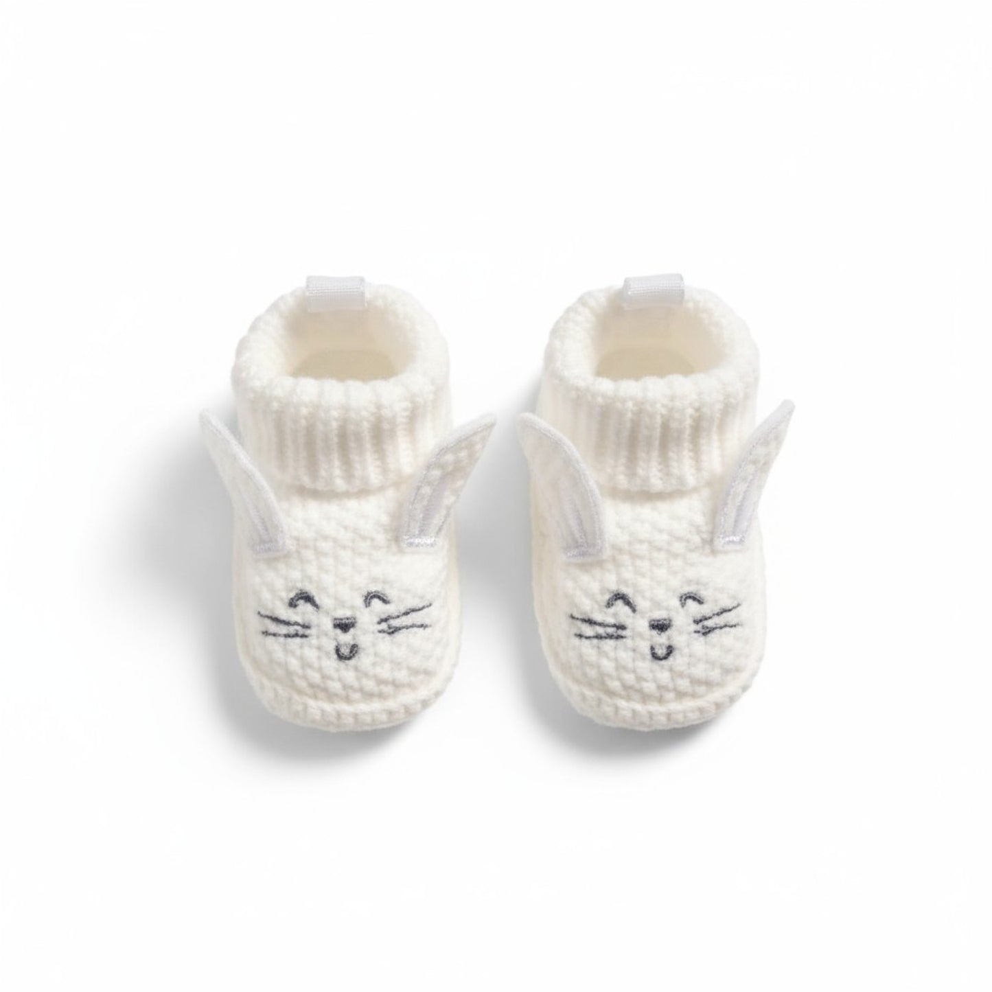Pair of white knit baby booties with bunny face design on a white background