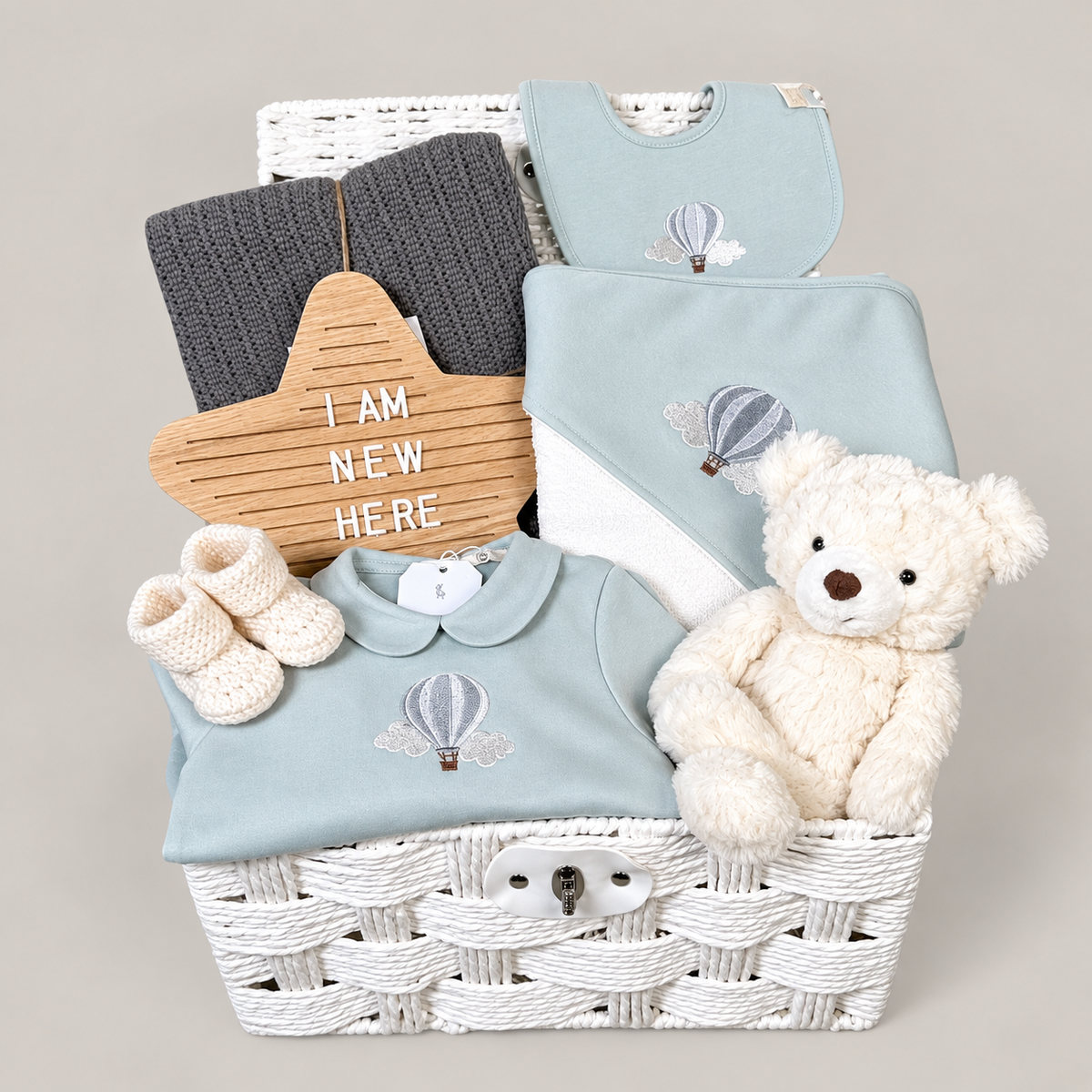 luxury baby hamper in a white paper rope hamper , with sage green baby clothing, hooded baby towel, baby blanket and baby booties