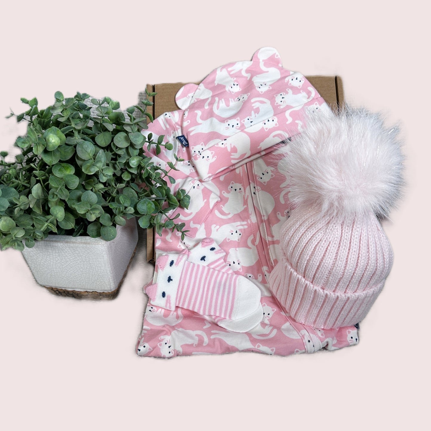 Baby girl hamper gift with pink zip up romper with a white kitty print and two baby hats.