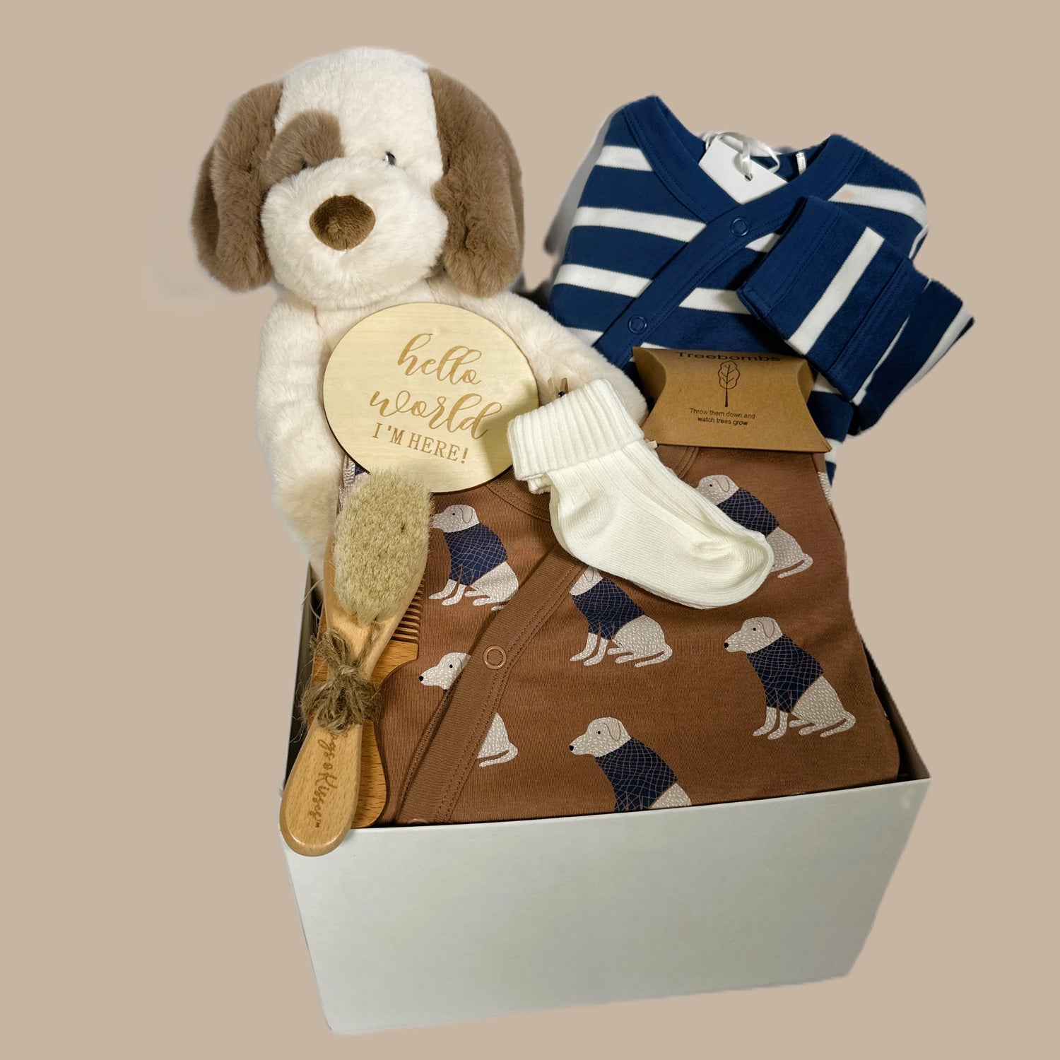 Baby hamper containing two organic cotton rompers with fold over cuffs and feet. One is a blue and white horizonal stripe and the other the same colours but with a labrador dog print. A baby brush and comb set and an Ebba Toddy dog soft baby toy.