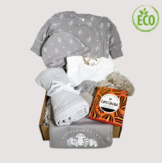 Unisex New baby gift withan organic cotton layette set in taupe and white, the bib reads "little and loved" in white print and the suit has a small repated toadstool pattern, a grey cellular baby blanket, a biscuit coloured baby pompom hat and a bar of Love Cocoa chocolate.