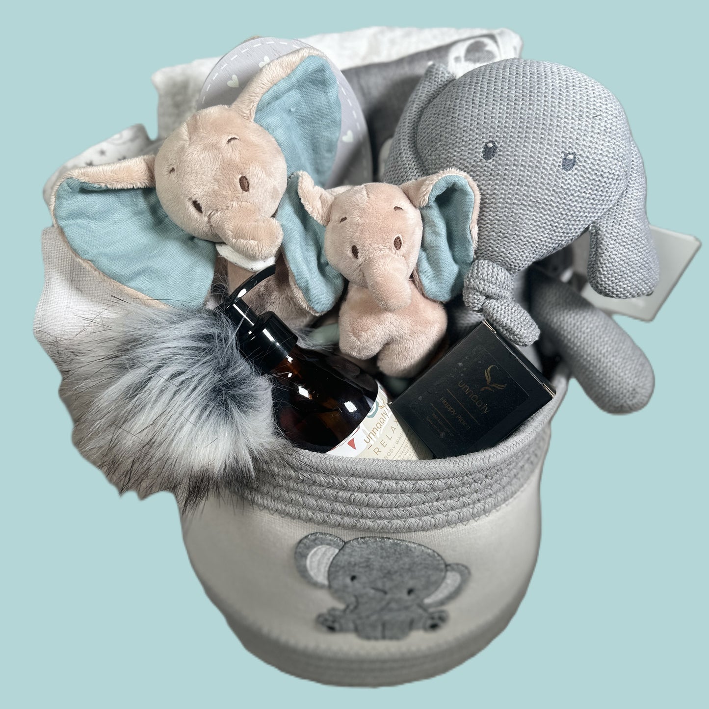 Baby gift basket with plush elephant toys and baby essentials on a light blue background