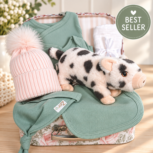 Baby girl hamper with sage green baby clothing, a pink pompom hat and piglet soft baby toy in a keepsake case.