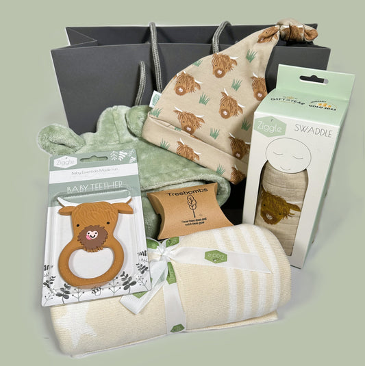 A new baby gift containing a cream and white cotton baby blanket , a highland cow print baby knot hat and baby swaddle. A highland cow silicone baby teether and a sage green baby dressing gown.