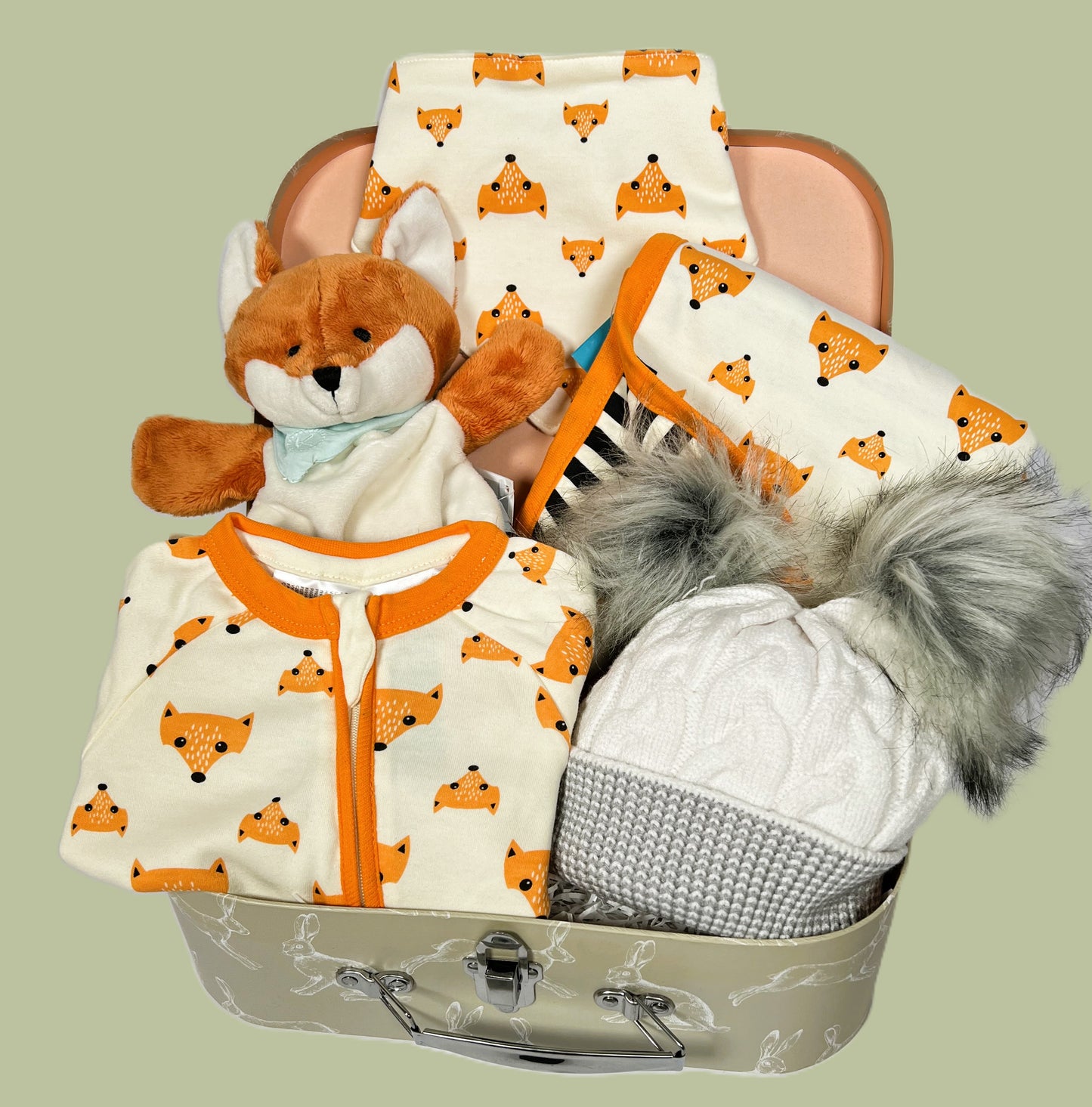 Baby hamper containing a cotton fox print zipped baby sleepsuit and matching dribble bib. A fox print baby blanket. A Kaloo fox baby comforter and puppet. A grey and white baby pompom hat in a sage green baby keepsake case.