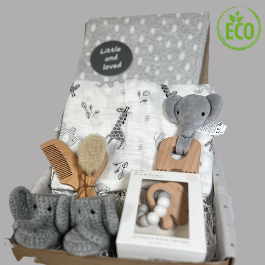 A stunning new baby hamper full of elephant baby essentials such aa a large white baby muslin with grey elephant and zebra print. Two elephant baby teething toys. A pair of crocheted baby booties with an elephant face, a grey organic cotton baby blanket and a baby hairbrush and comb set.