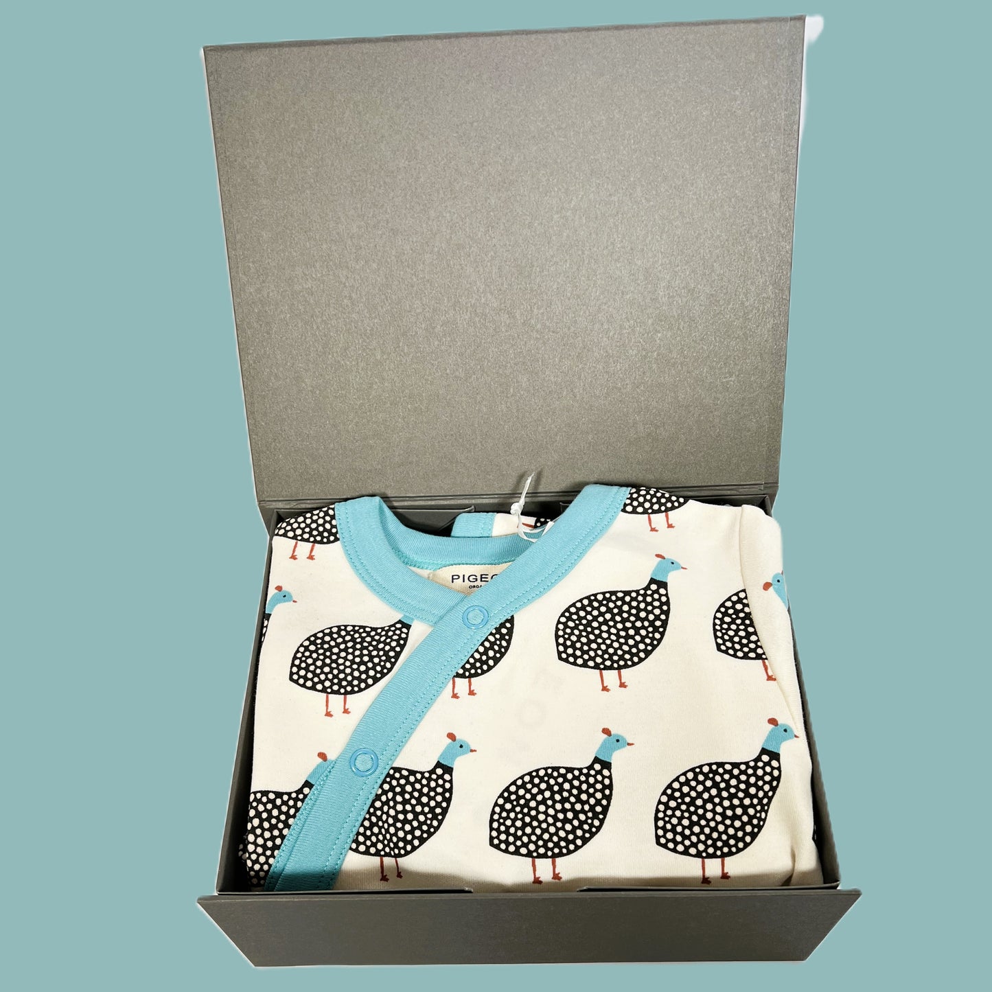 A baby shower gift in a magnetic gift box containing an organic baby sleeps suit in a Guinea fowl print with matching reversible baby dribble bib, A bar of Love Cocoa Malden sea salt dark chocolate, a taupe baby muslin and a taupe baby pompom hat.