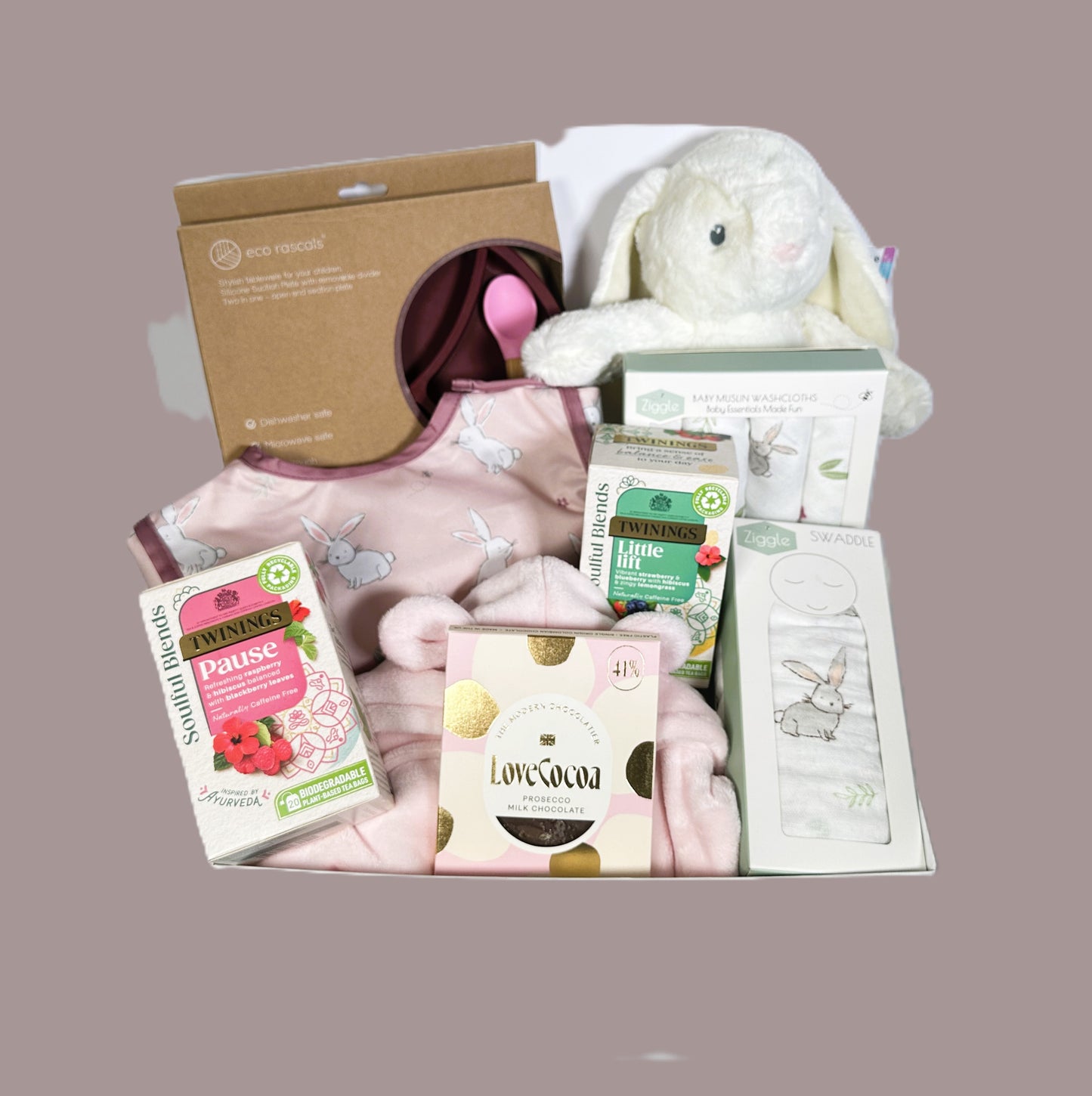 Baby girl hamper with pink baby dressing gown, baby coverall bib, Ebba bunny soft baby toy, Ziggle bunny print muslin swaddle and matching face cloths. An Eco Rascals silicone baby plate and bamboo spoon. Calming Twining teas.