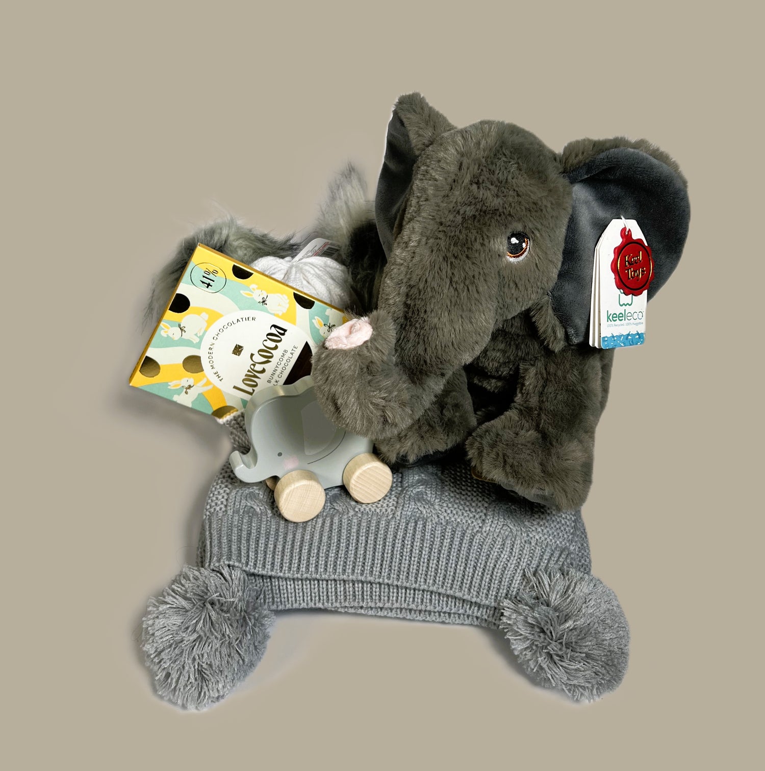 A baby shower gift in a baby keepsake box containing an Eco Cuddlies Wilberry elephant soft toy, a grey baby pompom blanket, a push along elephant toy, a bar of Love Cocoa chocolate and a grey and white baby pompom hat.