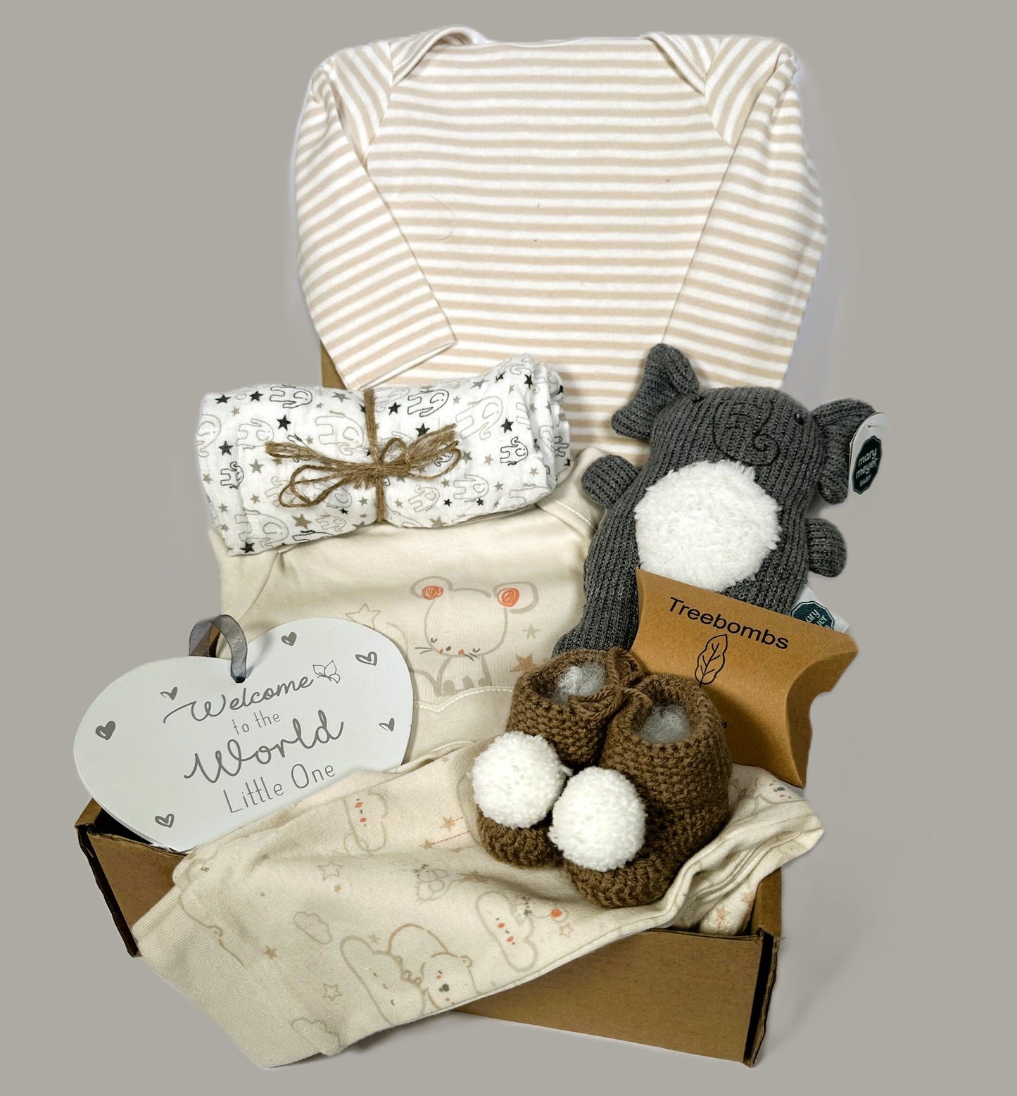 Elephant themed baby shower gift hamper containing  a Mary Meyer elephant baby rattle. A heart shaped nursery plaque. A pair of baby trousers and matching baby long sleeved t-shirt, a baby body suit.  matching band a pair of chrocheted baby booties with white pompoms.