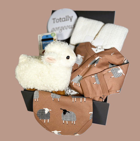 Baby shower gif of 1o organic cotton baby sleep suit and matching dribble bib in mocha with white and dark grey sheep print. A white cotton cellular baby blanket, A soft baby toy sheep and a packet of Twining "Peace" tea bags in a grey baby keepsake box.