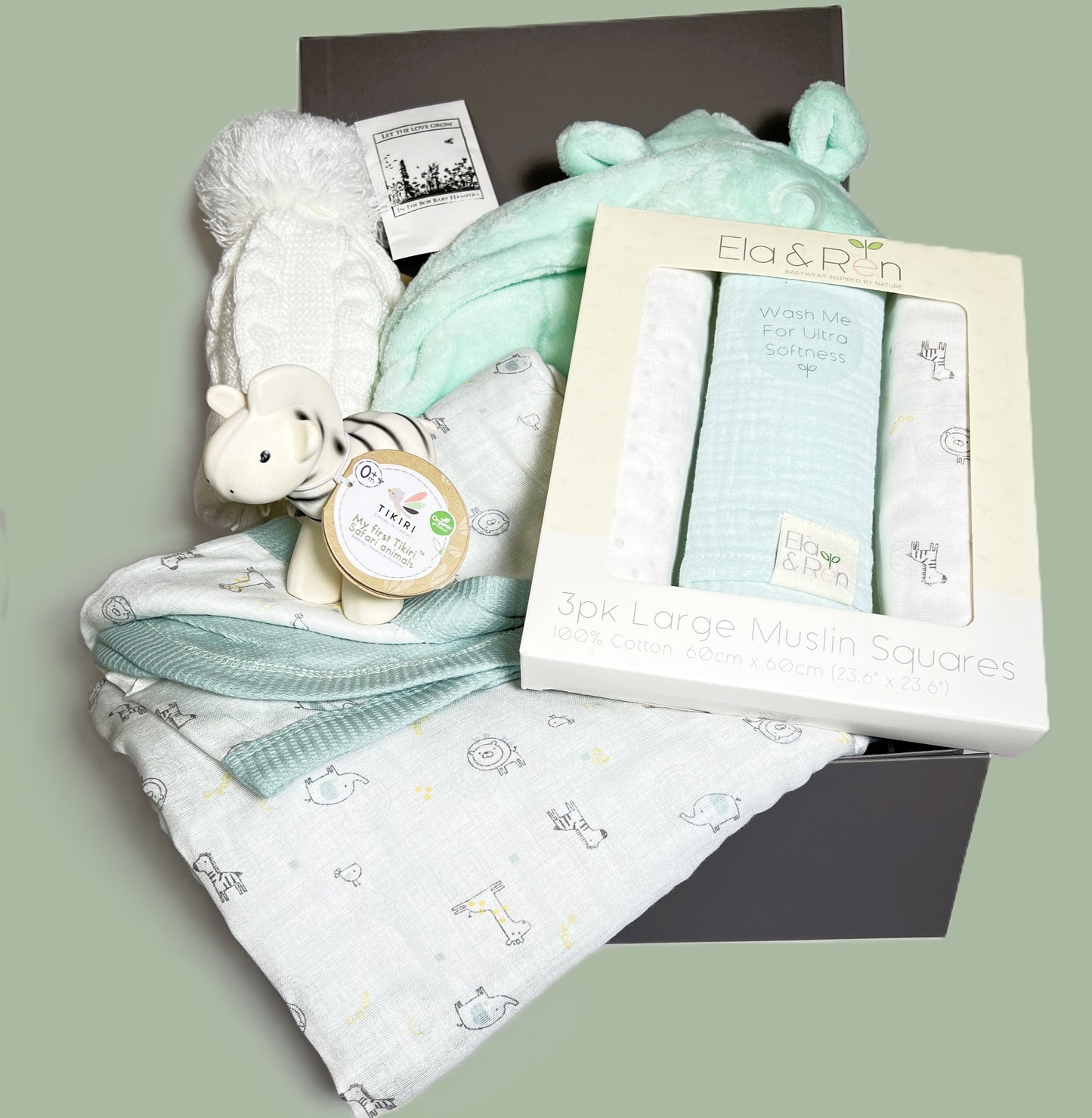 A baby hamper in a grey magnetic baby keepsake box containing a set of muslin squares and a matching cotton waffle baby blanket in a jungle print with a set of three matching baby muslin. A Tikiri organic rubber zebra baby teether/rattle. A mint coloured baby dressing gown and a white baby pompom hat.