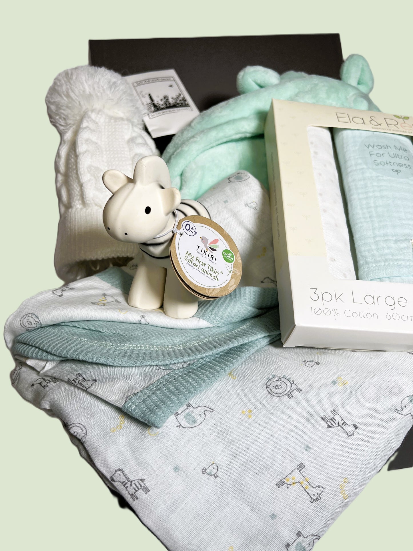 A baby shower gift in a grey magnetic baby keepsake box containing a muslins and cotton waffle baby blanket in a jungle print with a set of three matching baby muslin. A Tikiri organic rubber zebra baby teether/rattle. A mint coloured baby dressing gown and a white baby pompom hat.