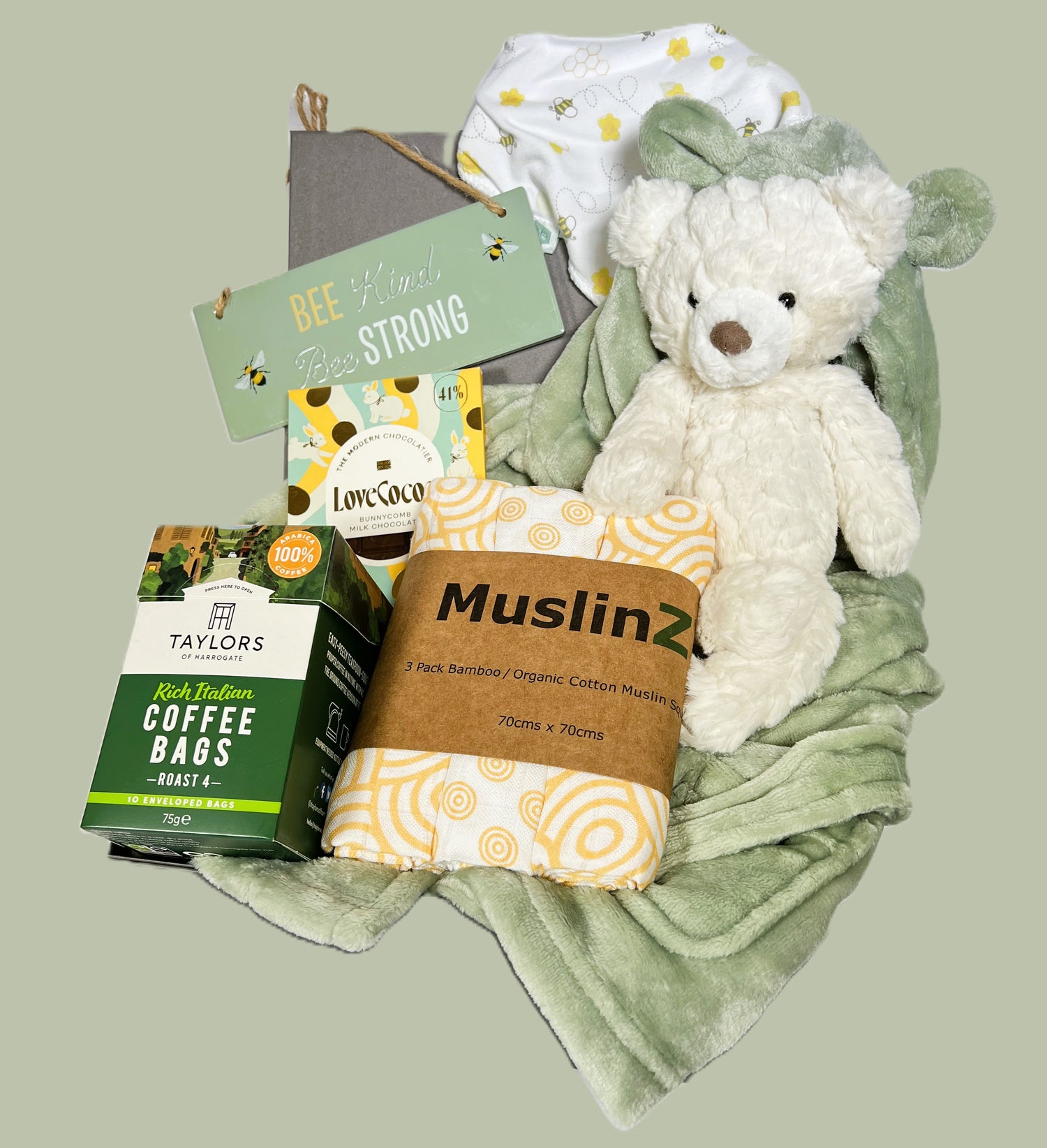 a baby shower hamper ith a sage breen baby dressing gown, a cream Mary Meyer teddy bear a pack of 3 Muslinz  baby muslin squares, a baby dribble bib with bee print, a pack of coffee bags and a bar of Love Cocoa chocolate in a grey baby keepsake box.