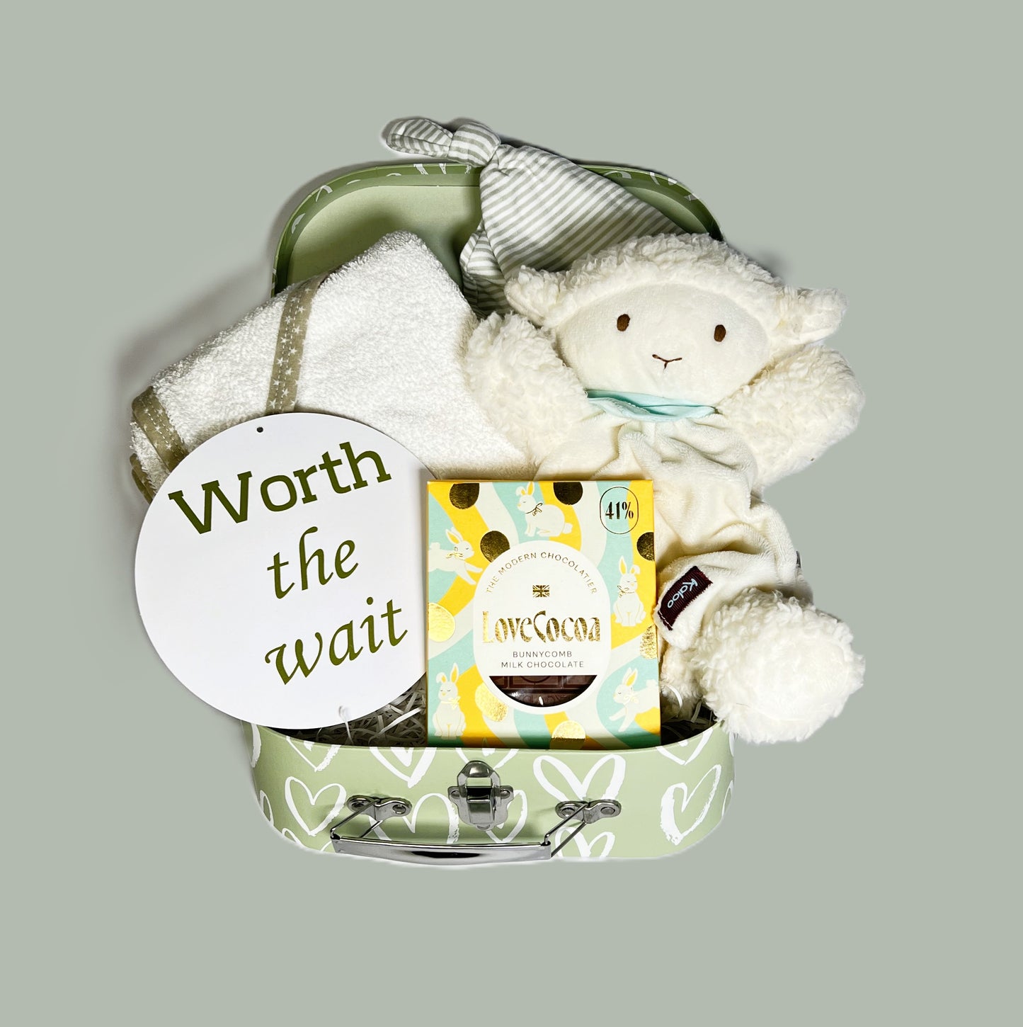 Baby shower gifts in a baby keepsake case containing a Kallo Vanilla lamb baby comforter which is also a puppet. A cotton hooded baby towel, a striped n cotton baby knotty hr and a bar of Love Cocoa "Bunnycomb" milk chocolate