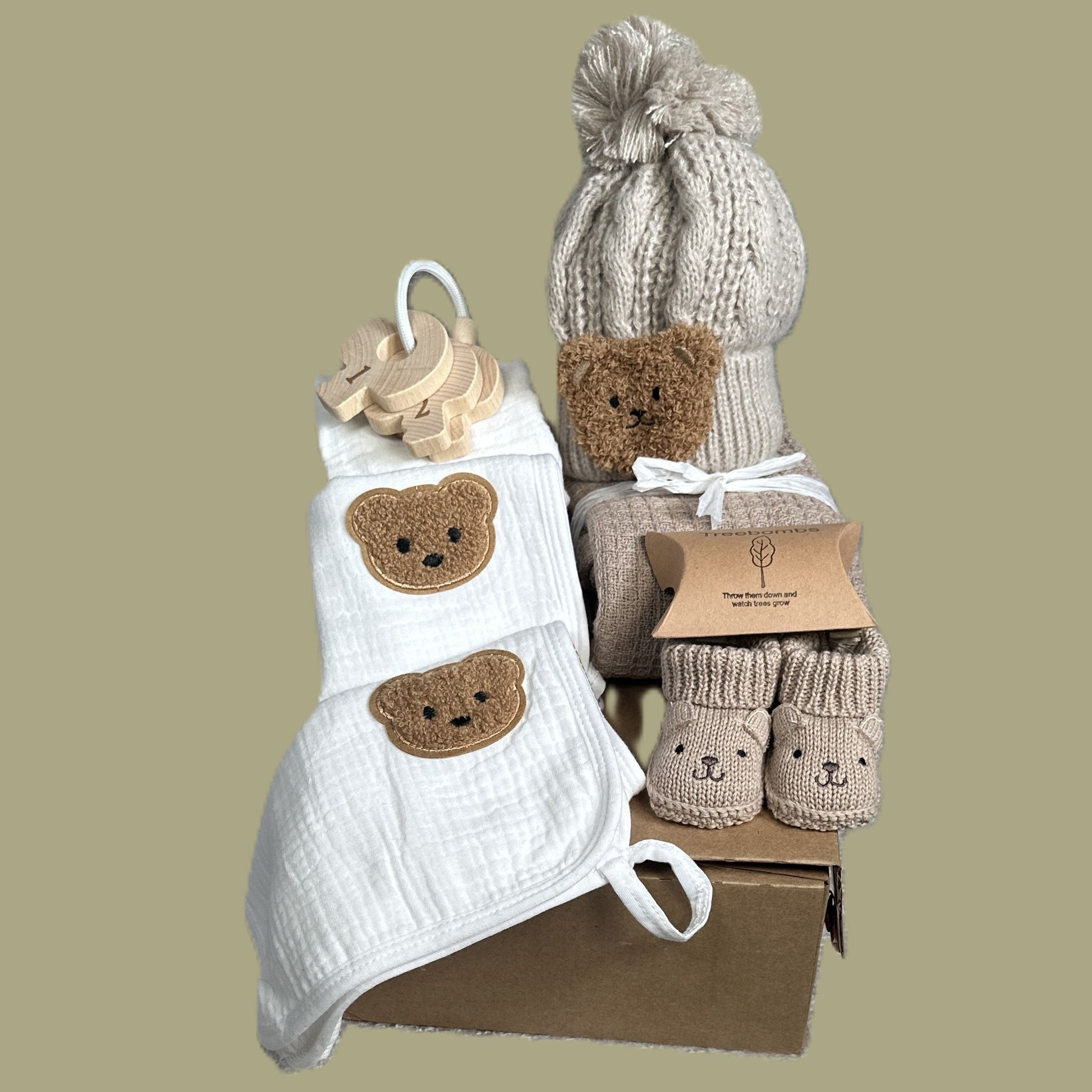 Baby gift set with white bib, hat, and booties on a beige background