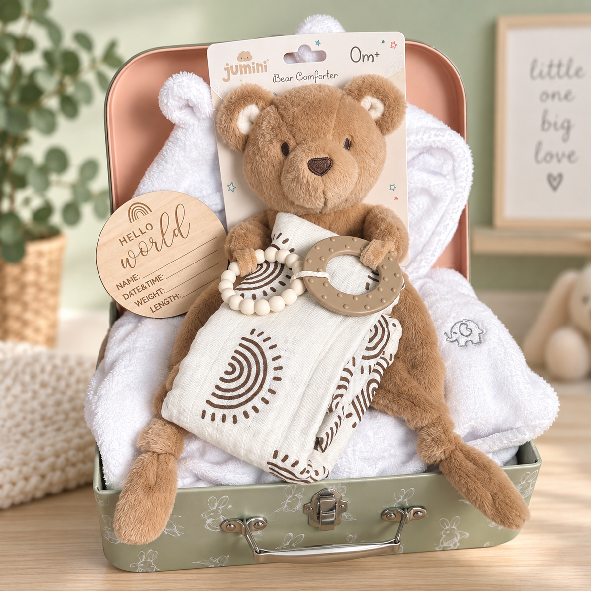 A teddy bear baby hamper in a vintage-style baby keepsake case. The set includes a plush brown teddy bear baby comforter with two silicone teething rings, muslin cloth with brown geometric sun print, a white baby robe,  and a wooden new baby announcement disc.