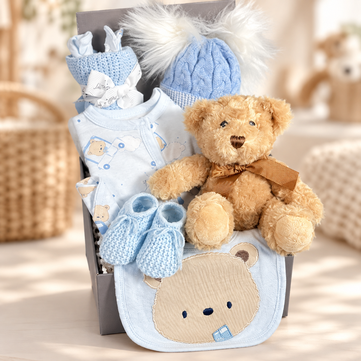 A baby hamper for a boy in a square grey magnetic baby keepsake box containing a blue bear print cotton layette set including a romper suit, baby hat, bodysuit and scratch mitts. A double pompom blue baby hat, a white muslin square a blue cotton cellular baby blanket and a Keeleco Dougie bear with a pair of blue baby bootees.
