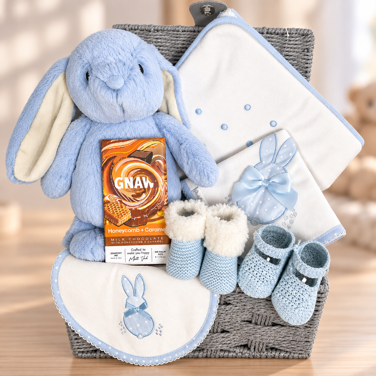 A grey rope baby hamper with a Ebba blue bunny soft baby bunny, a white cotton hooded baby towel, matching bib and burp cloth and booties.