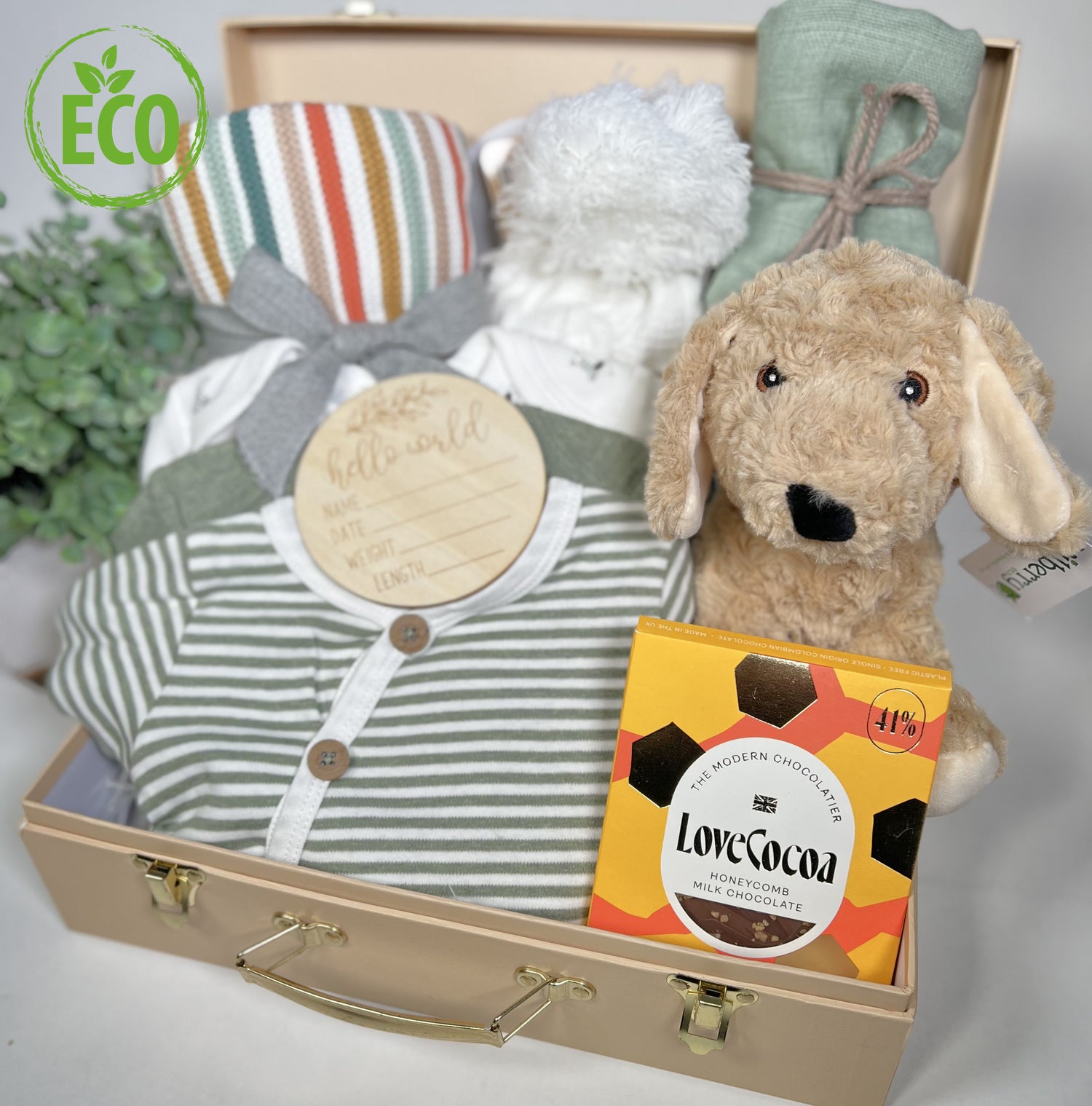 Unisex baby gift haper full of eco friendly new baby essentials including a 3 piece organic set of baby body vests in green abd white, a green muslin square, a cotton striped baby blanket, a baby pompom hat, a bat of LOve Cocoa chocolate and a cockapoo soft toy made from recycled plastics.