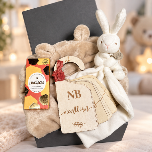 A gift box containing a cream bunny baby comforter teddy bear plush toy, a Gnaw chocolate bar, and baby wardrobe dividers in a dark grey box.