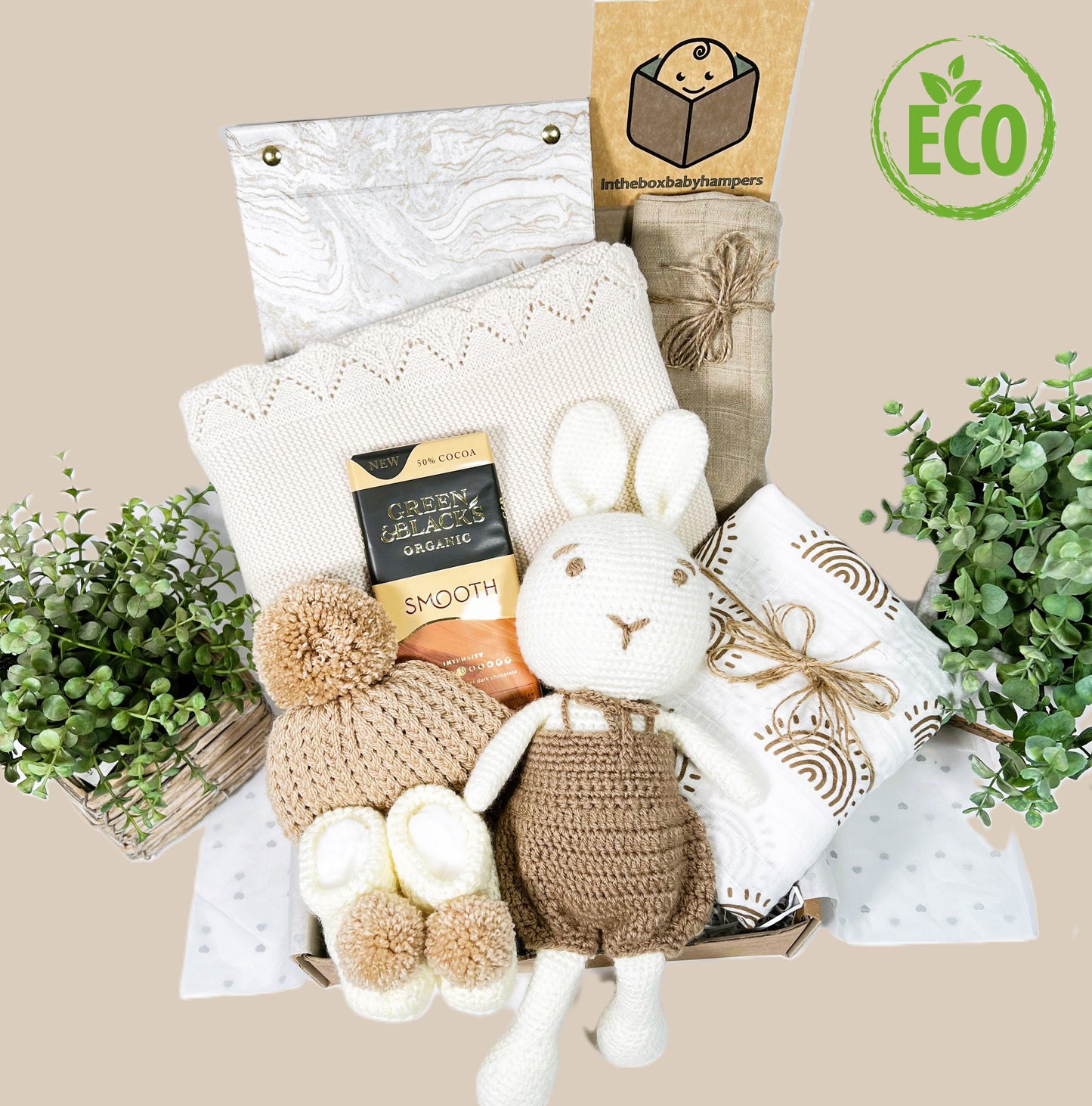 Eco Friendly neutral new baby gift hamper box with a crocheted bunny in brown dungarees abd a hand stitched face, a soft cotton baby blanket, a large white muslin with brown printed suns, a pair of cream crochetd baby booties and knitted baby pompom hat.