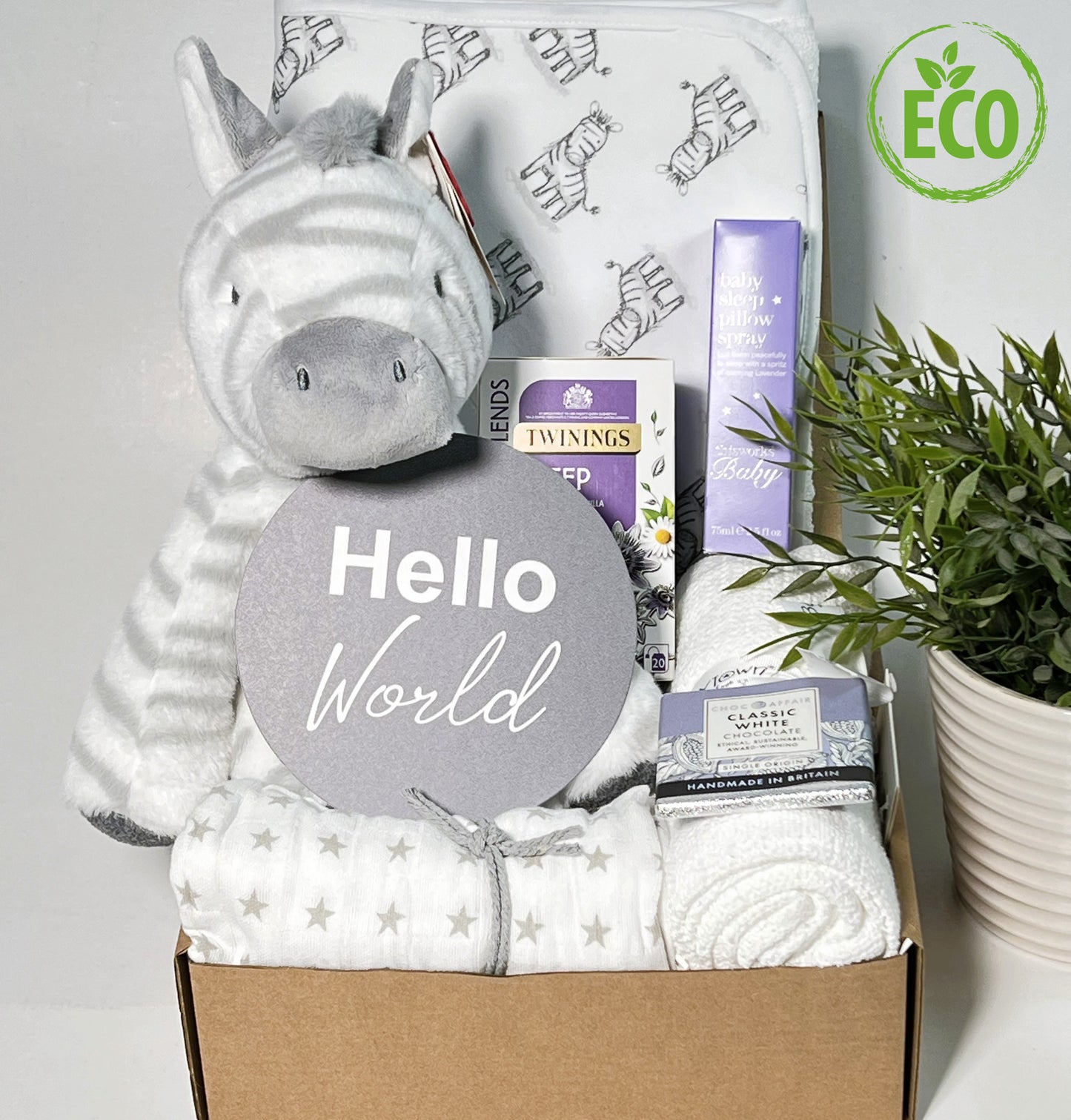 Unisex eco friendly new baby hamper containing a zebra print hooded baby towel, a zebra soft baby toy, a white cellular baby blanket, a bottle of "This Works" baby pillow spray, a packet of Twining "Sleep" teabags and a bar of chocolate.