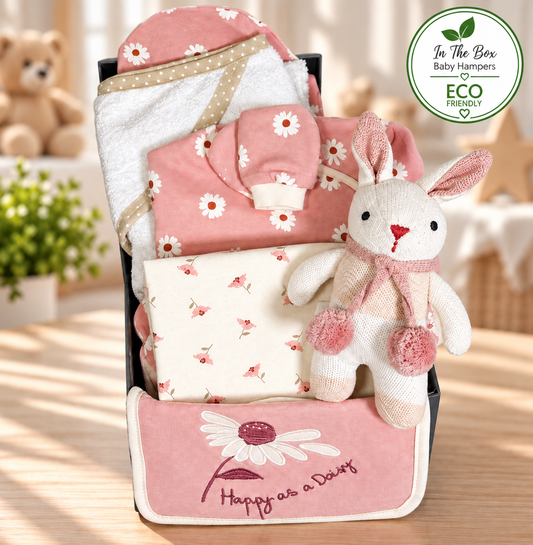 A new baby girl hamper in a grey baby keepsake box containing a pink and white organic cotton layette set with a white daisy print, a cotton hooded baby towel and an organic cotton bunny baby rattle.