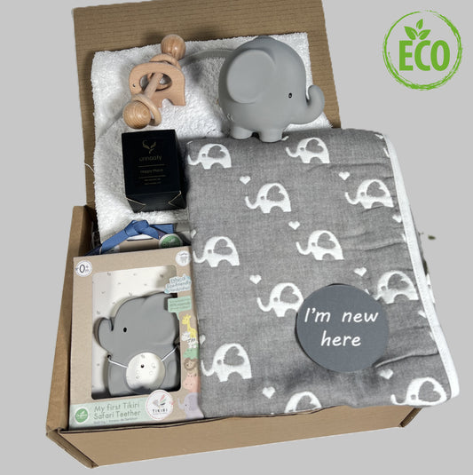 Grey and white new baby gift containing a white elephant print, a Tikiri elephant baby bath toy and e, a white cotton hooded baby towel and a Montessori elephant baby rattle.