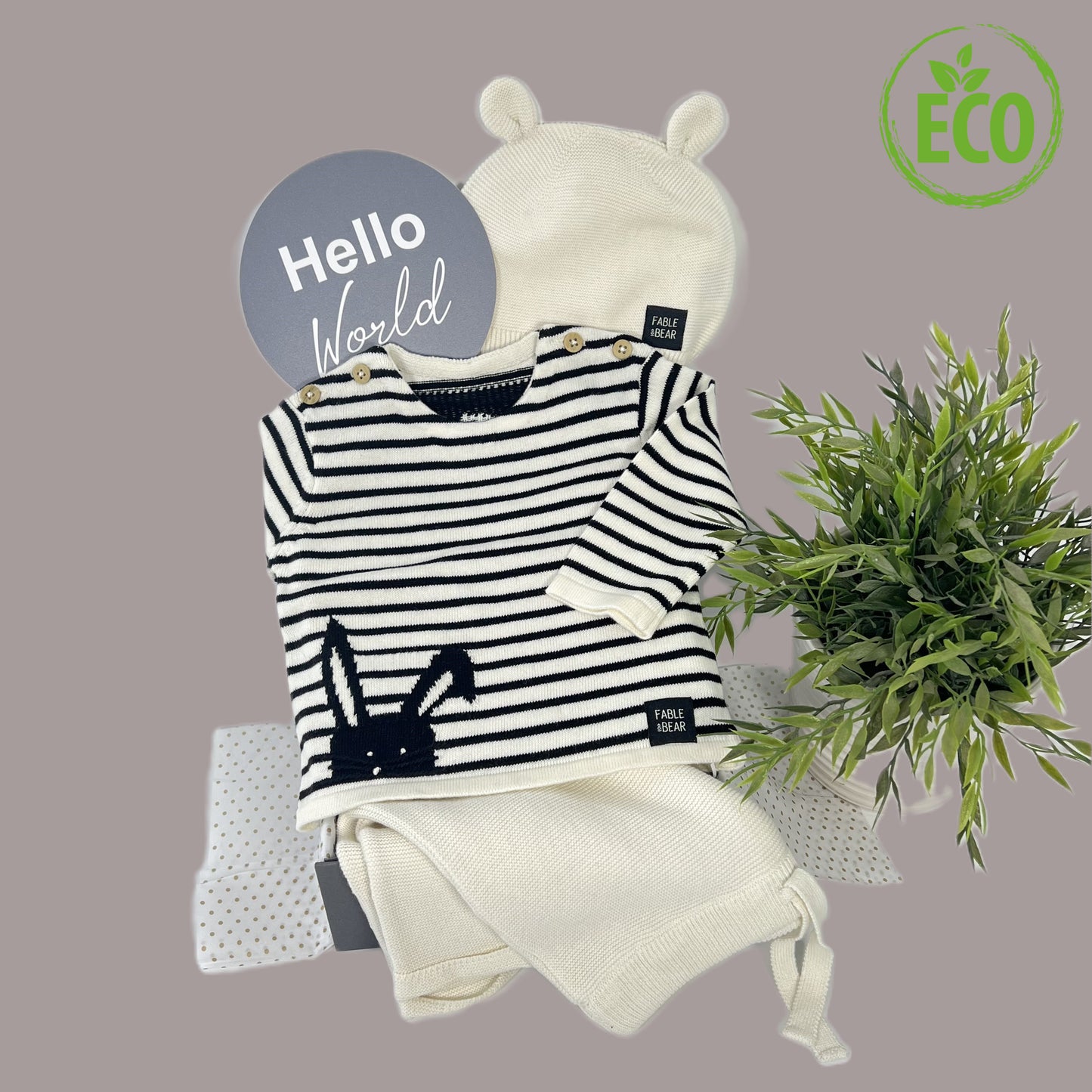 This luxury neutral new baby gift organic cotton baby clothing set , a baby jumper with a bear face and hand stitched facial features, a matching baby hat and baby leggings, a cotton baby cellular baby blanket, a elephant Montessori baby rattle in beech , a lage "Hello world " photography disc and a white baby keepsake box.
